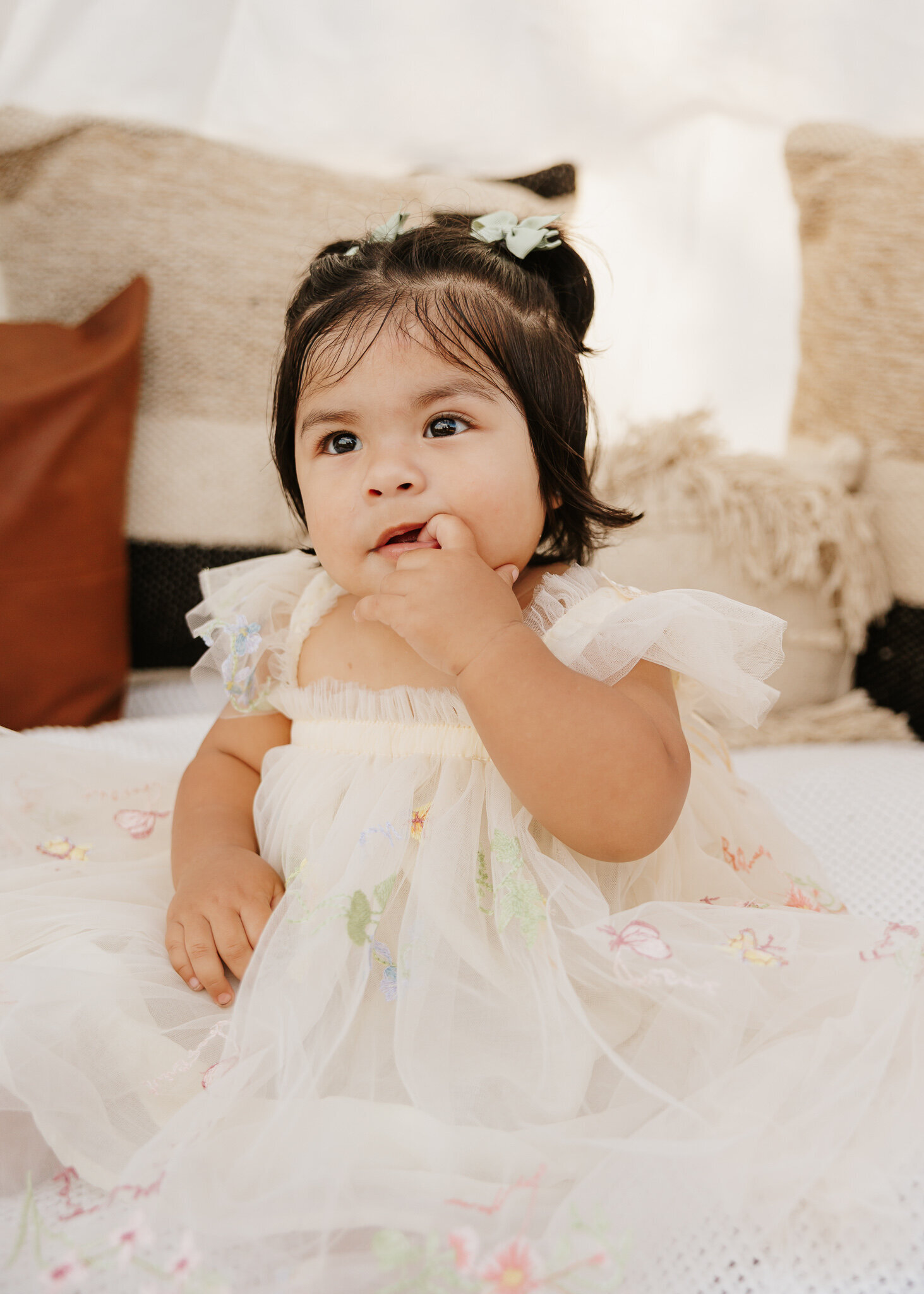 First birthday photoshoot in Aiken SC - baby girl in a cream dress sitting indoors with soft natural light and neutral decor.