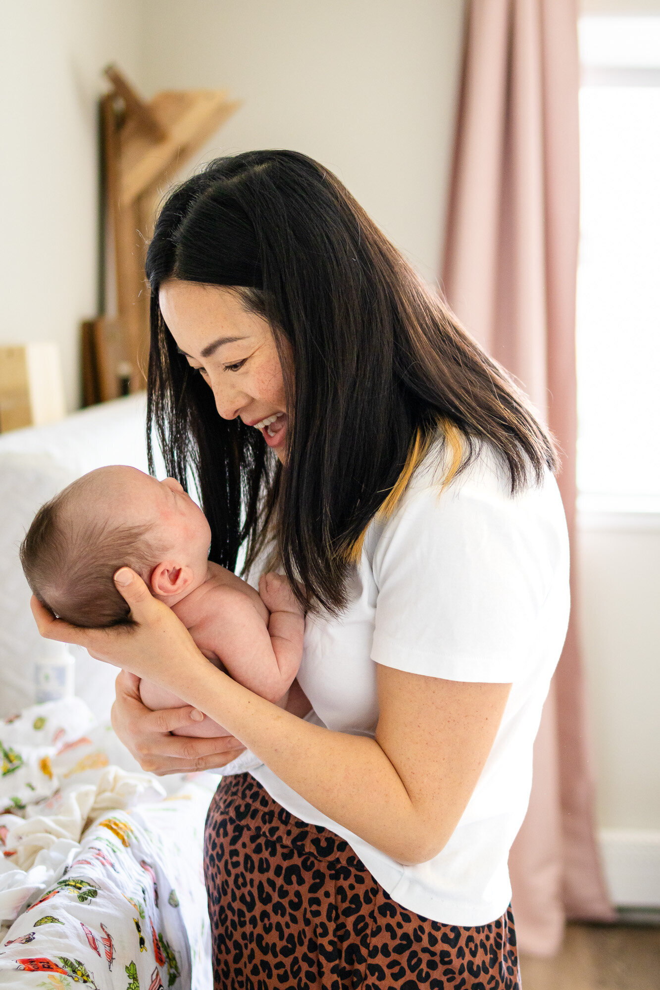 Joyful mother holding newborn face-to-face in bright nursery, photographed by San Francisco newborn photographer.