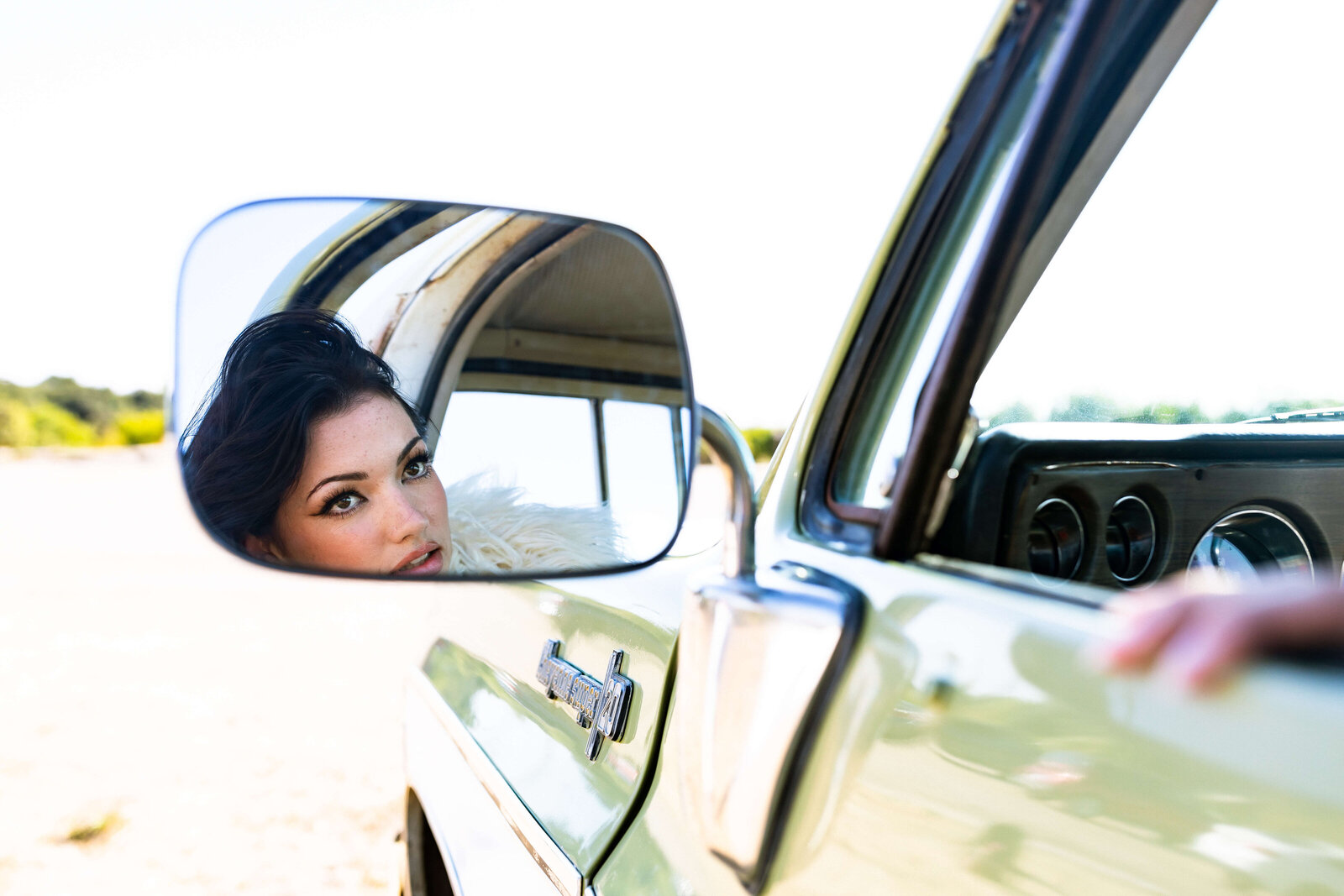 brunette girl looking into a car side view mirror in old green vintage truck