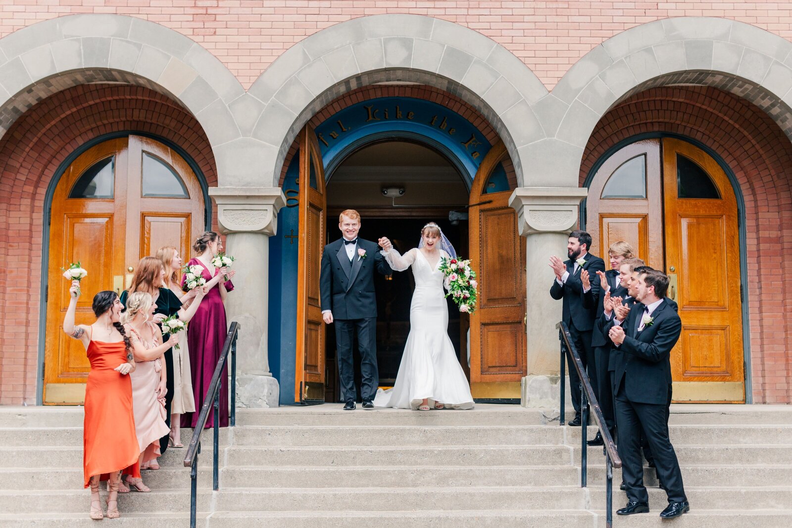Catholic bride and groom joyfully exit their wedding ceremony at Saint Thomas the Apostle Church in Coeur d’Alene as their fall-themed bridal party cheers them on—captured by Coeur d’Alene wedding photographer Sarah Noel