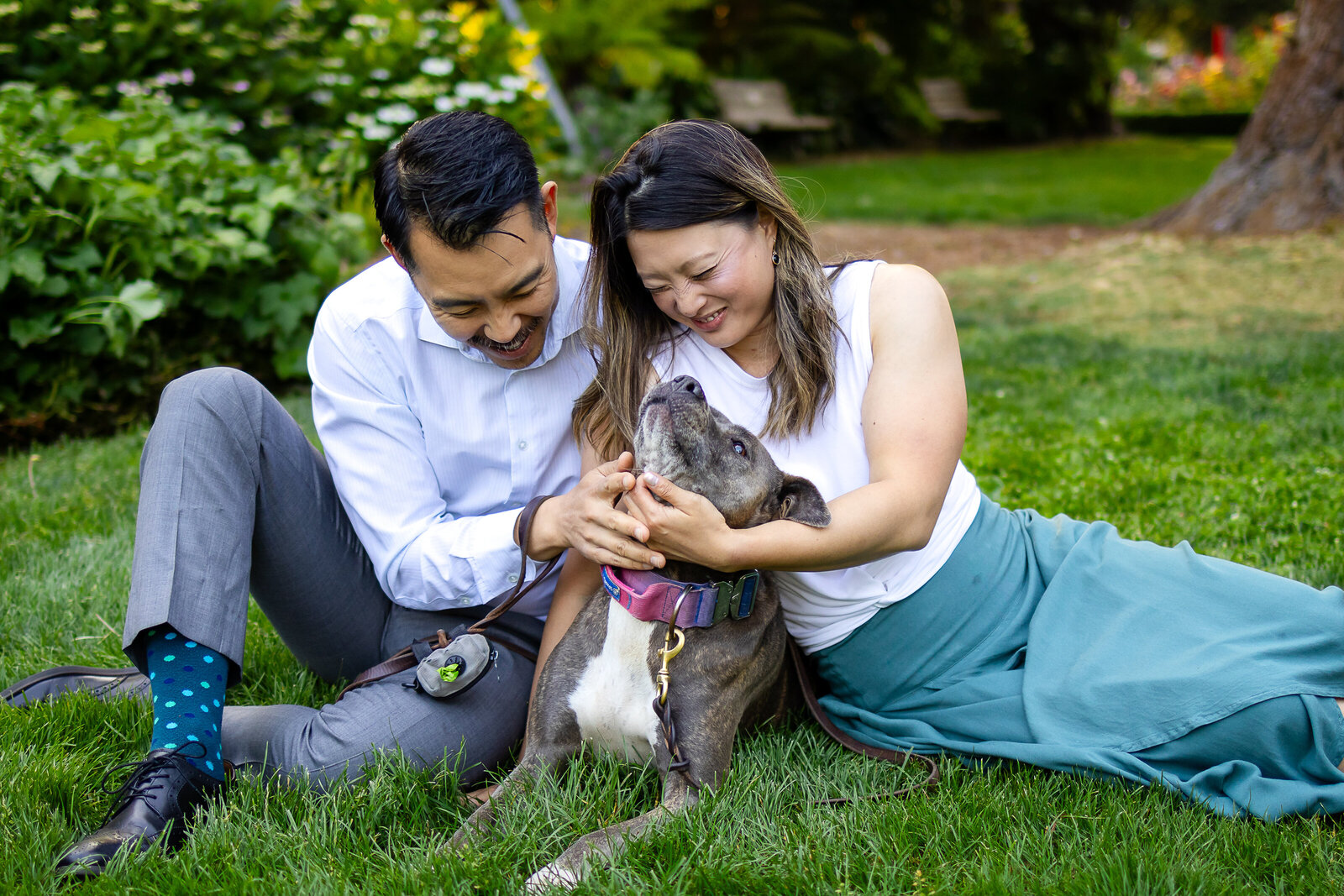 A couple shares laughter while sitting in the grass with their beloved dog, a candid moment by Ellobelle Photography.