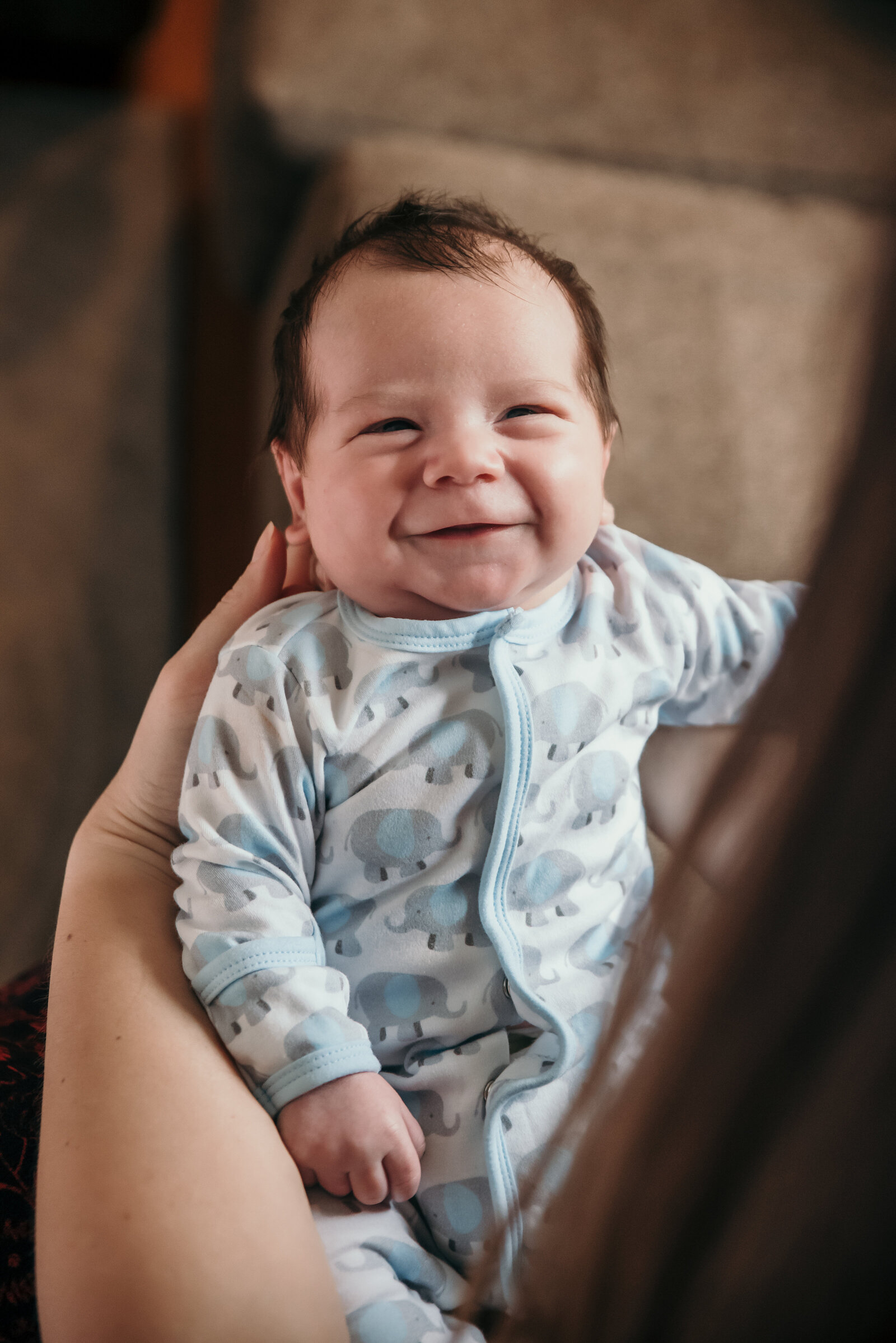 Celebrate the sweetest moments with natural, heartwarming newborn photography in Connecticut. This image captures a beaming baby in a cozy home setting, highlighting the joy and warmth of early parenthood. Book a lifestyle newborn session to document your little one’s first smiles and milestones with timeless, candid photography.