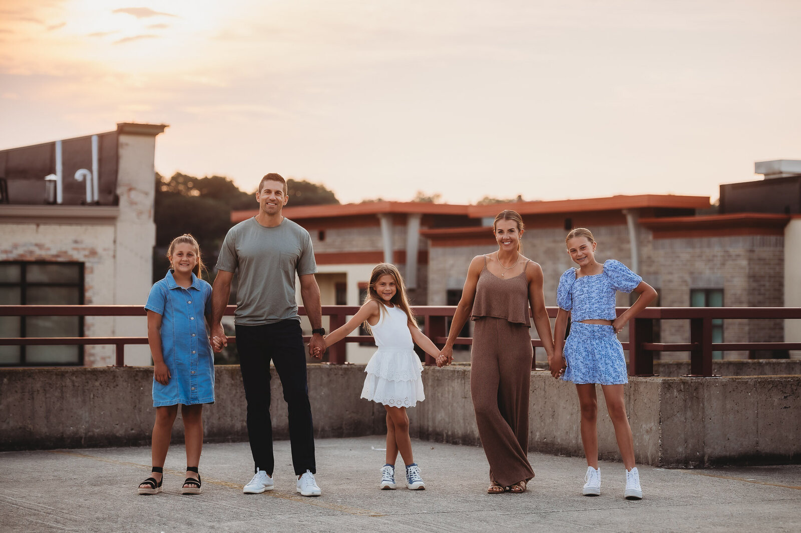 Family of 5 standing smiling and holding hands in a line on top of a parking garage
