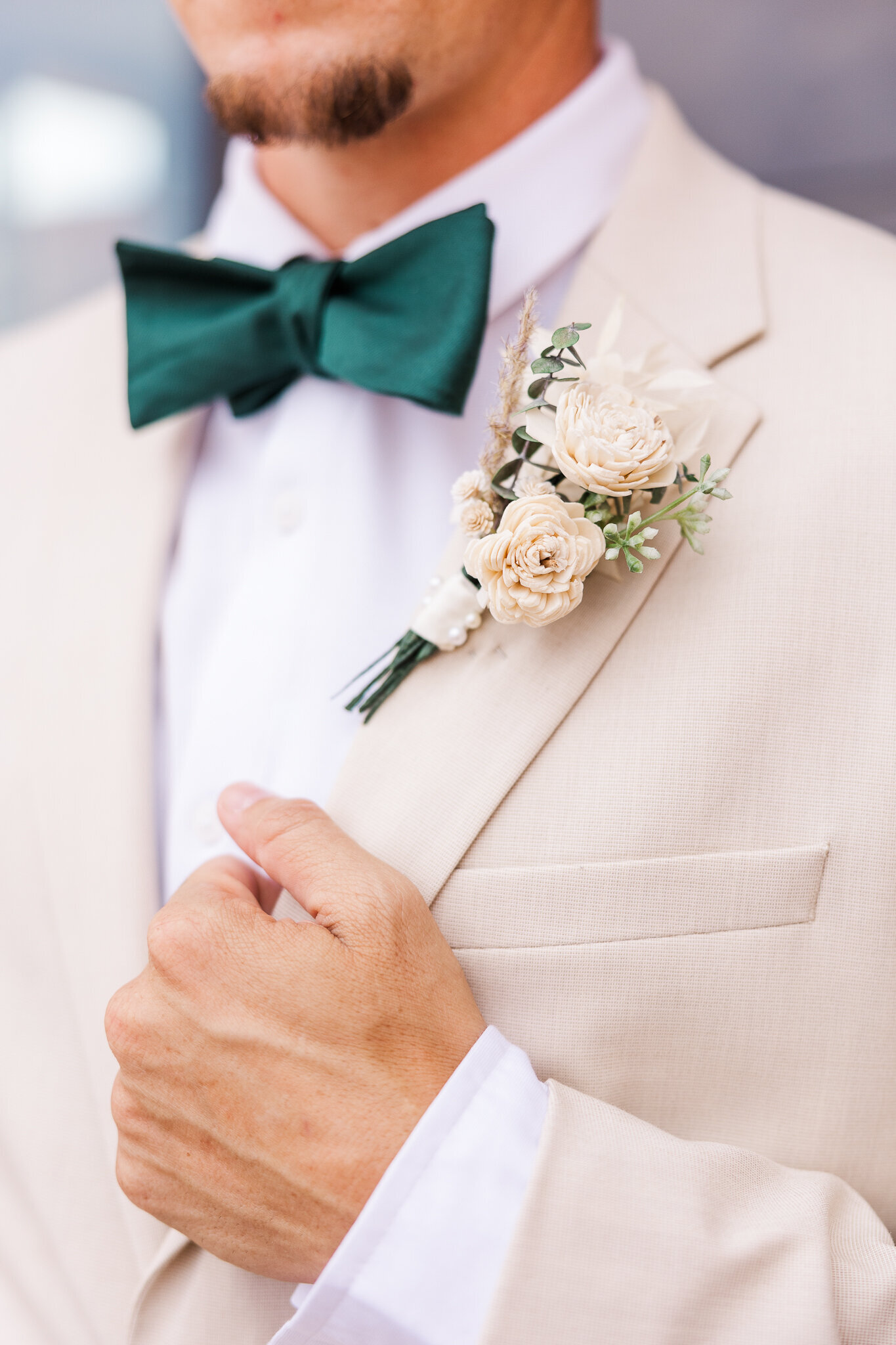 Groom holding on to his lapel with his boutonniere before wedding day in white suite 