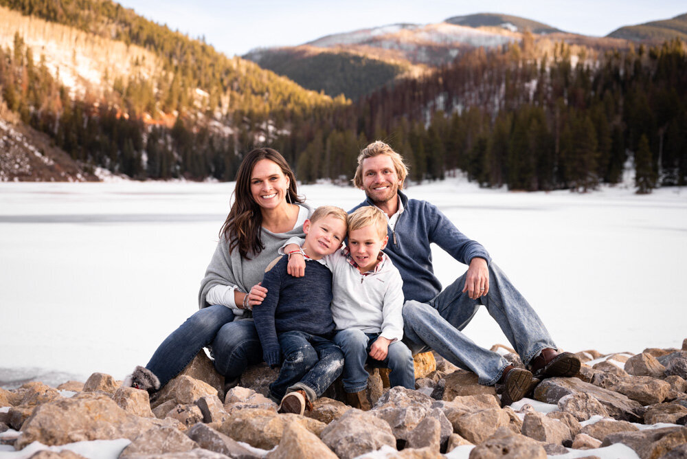 A family of four sits by the lake and smiles at the camera together