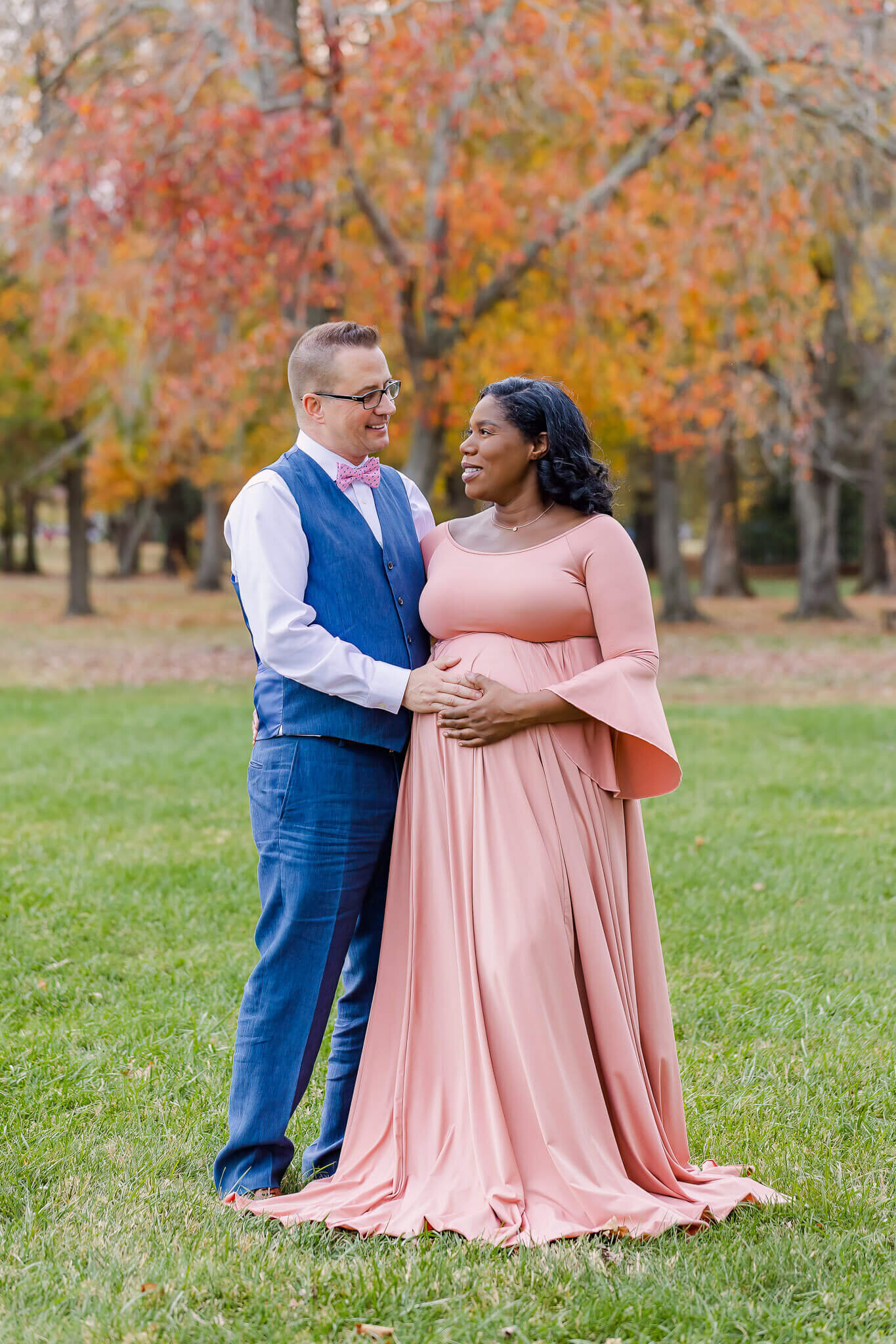 An expecting couple posing in a field for a maternity portrait session.