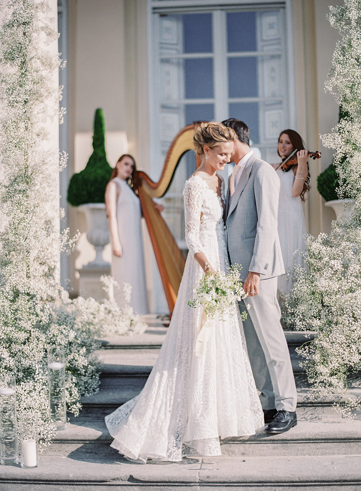 Groom whispering to bride during ceremony on front steps of villa. Harpist and violinist in the background. Photographed by Italy wedding photographer Amy Mulder Photography