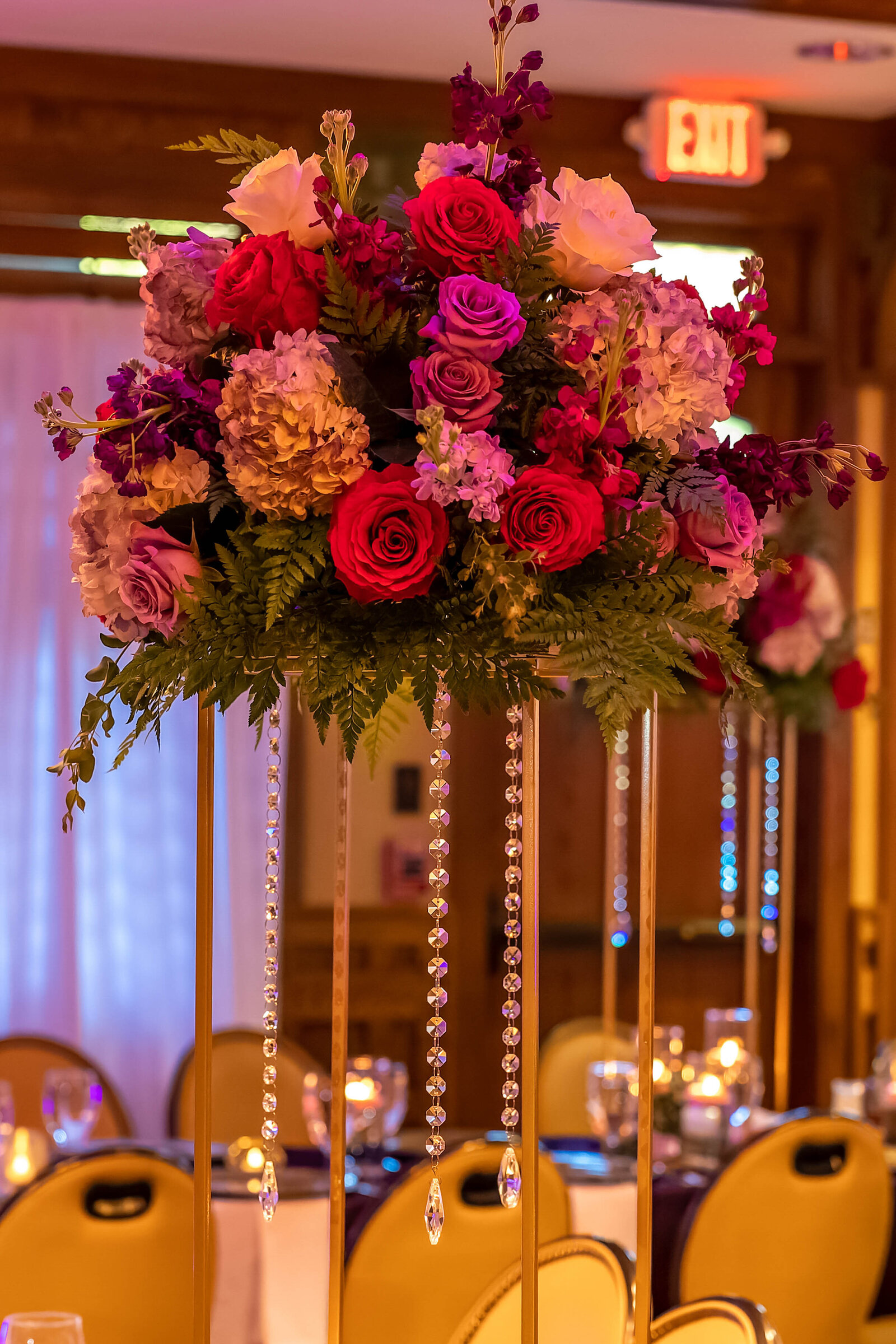 An elevated wedding centerpiece with vibrant roses, hydrangeas, and hanging crystal strands decorates a reception table, captured during an elegant Chetola Resort wedding in Blowing Rock, NC.