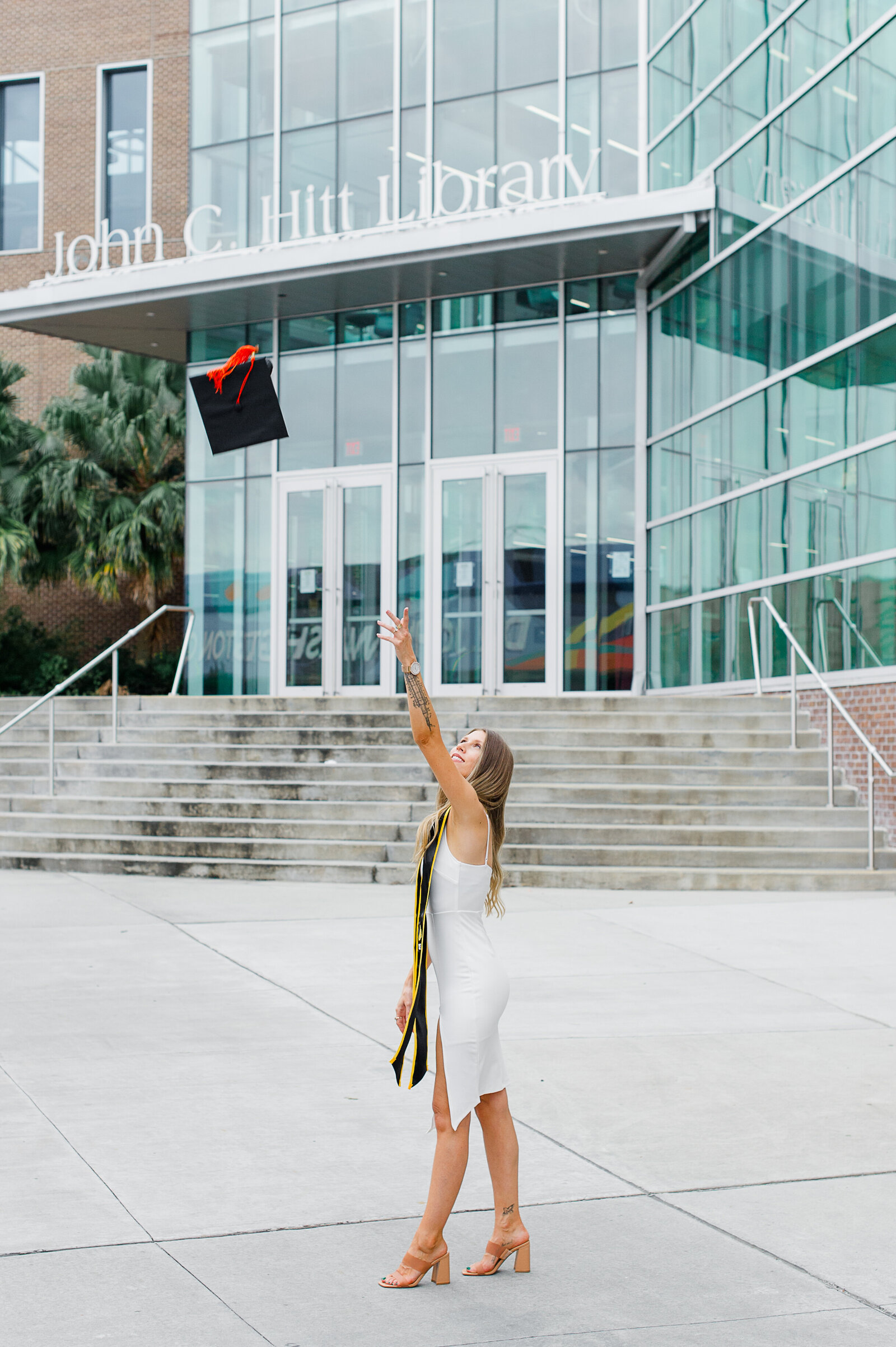 UCF senior girl stands in front of Joh C Hitt Library and throws her cap
