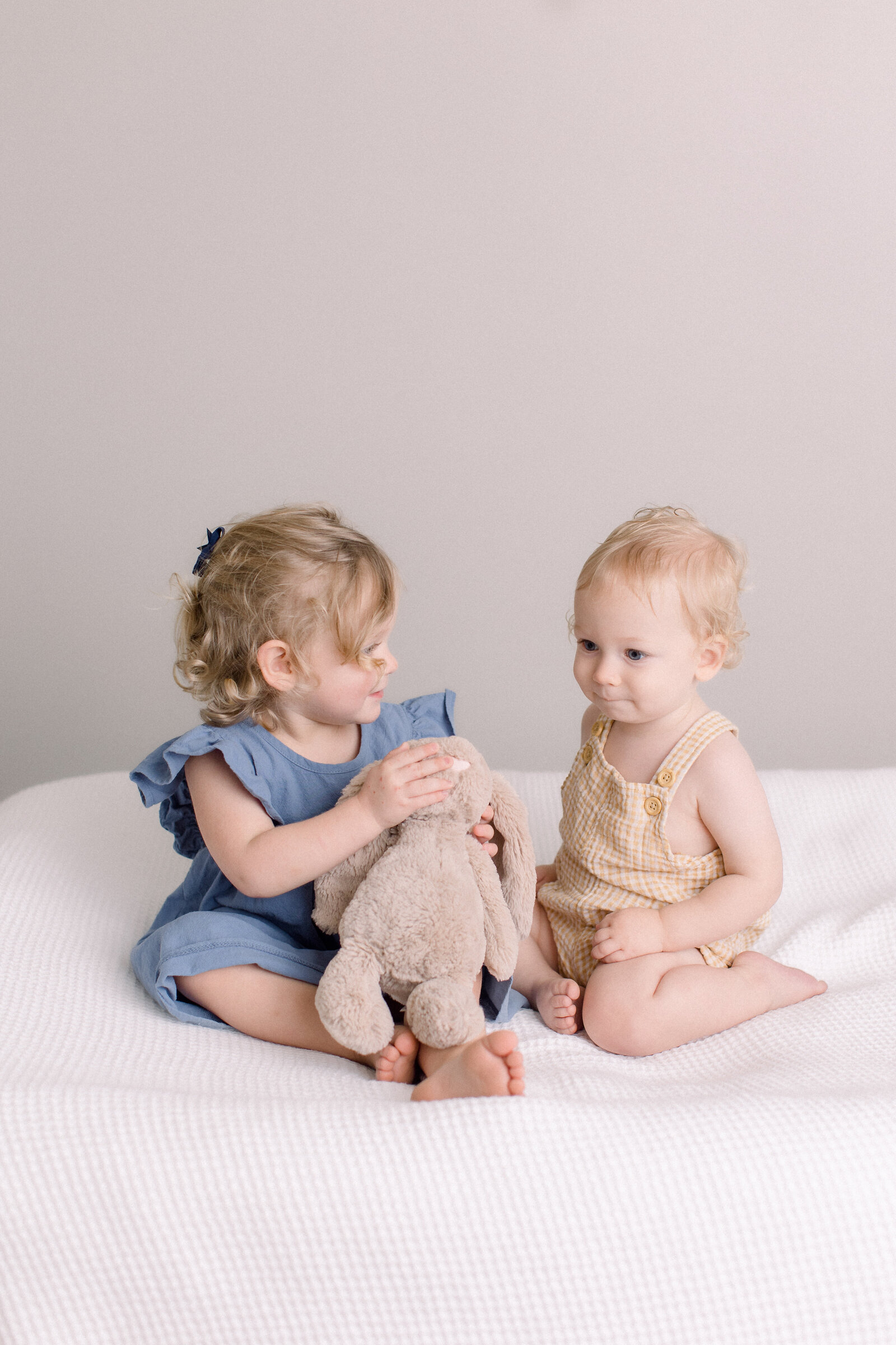 Two toddlers sitting on a bed playing with a stuffed bunny by NH newborn photographer Fieldstone Studio.