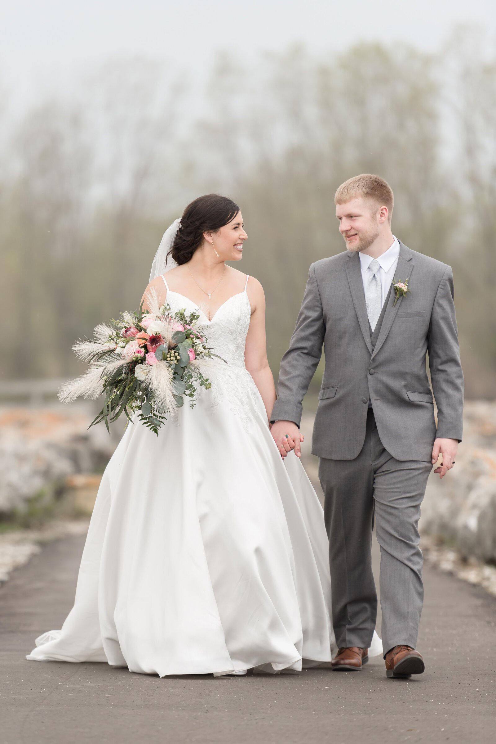 couple looking at each other while holding hands walking down pathway by Lake Huron