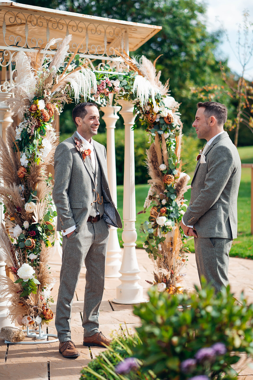 groom-waiting-under-floral-arch-during-outdoor-cheltenham-wedding