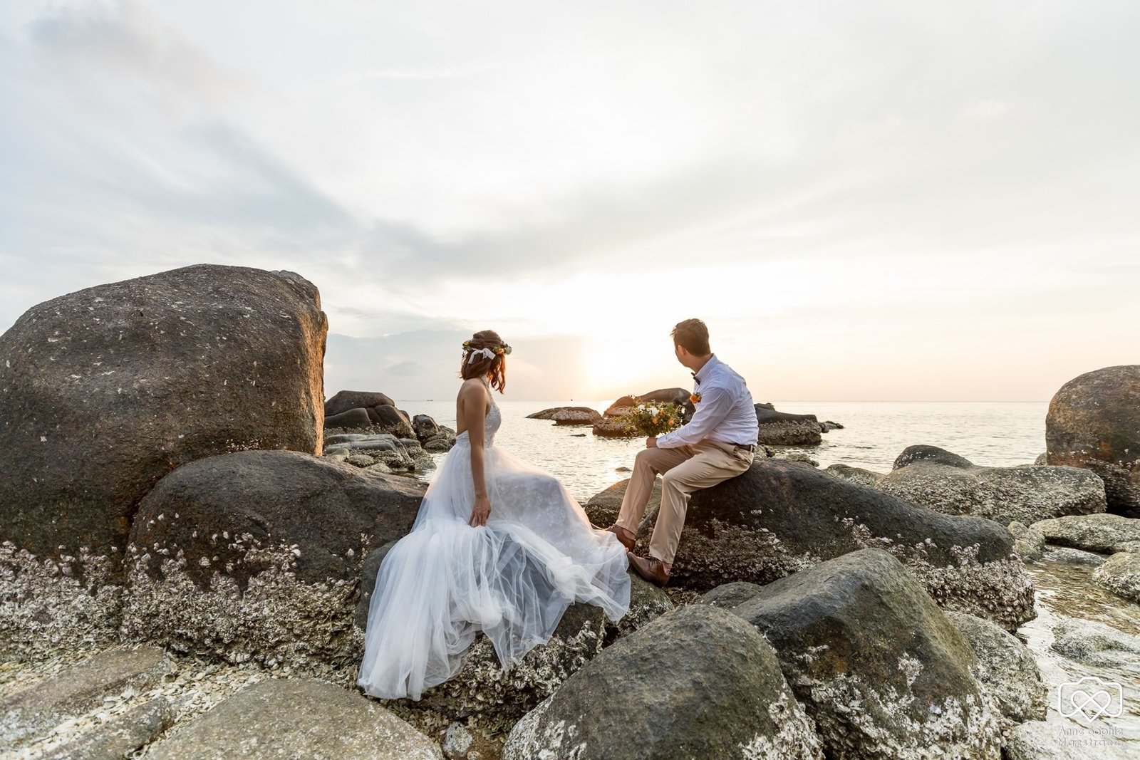 bride and groom sitting on rocks at Sai Nuan beach