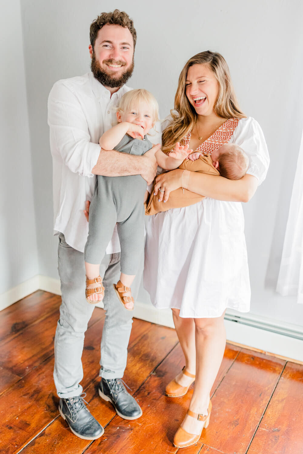 Mom, dad, and toddler laugh with a newborn in mom's arms