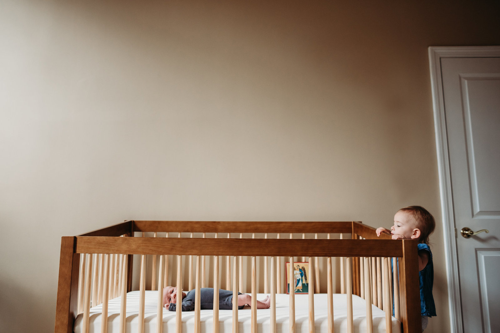 toddler peeks over side of crib at baby brother
