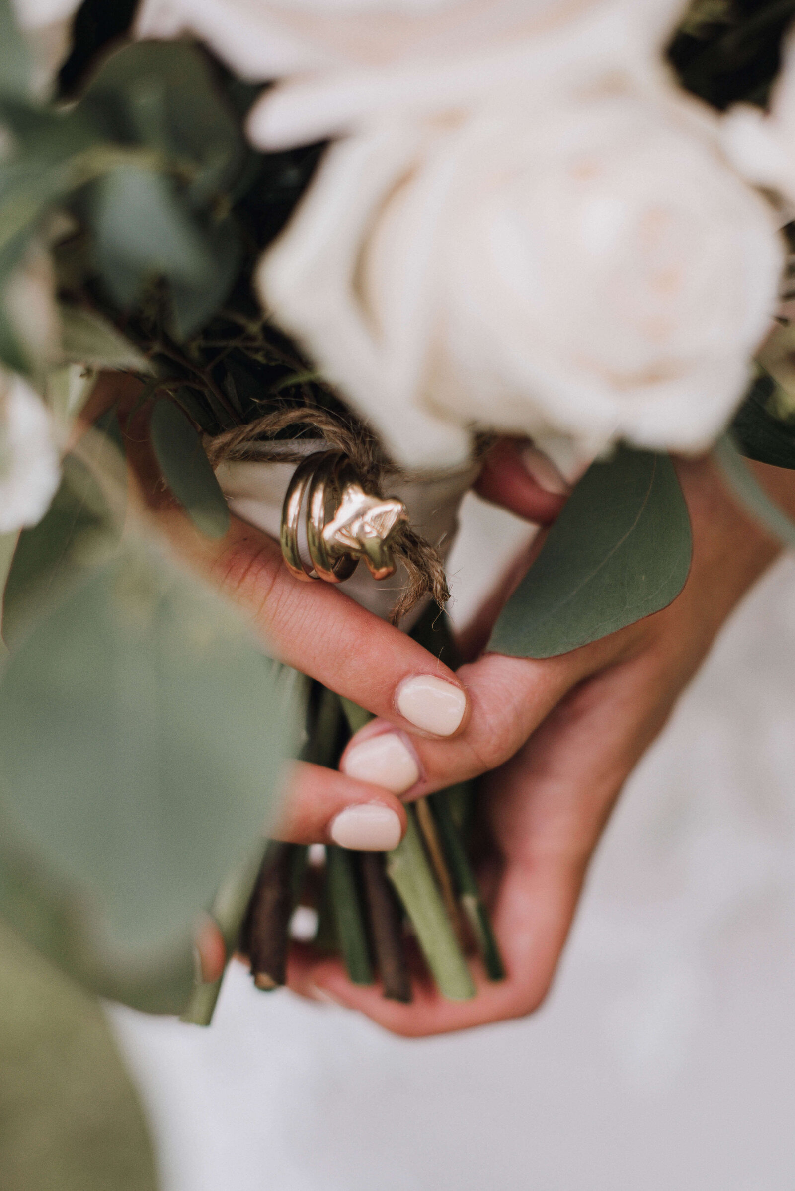 Detail of a brides hands holding a bouquet with rings tied to the handle