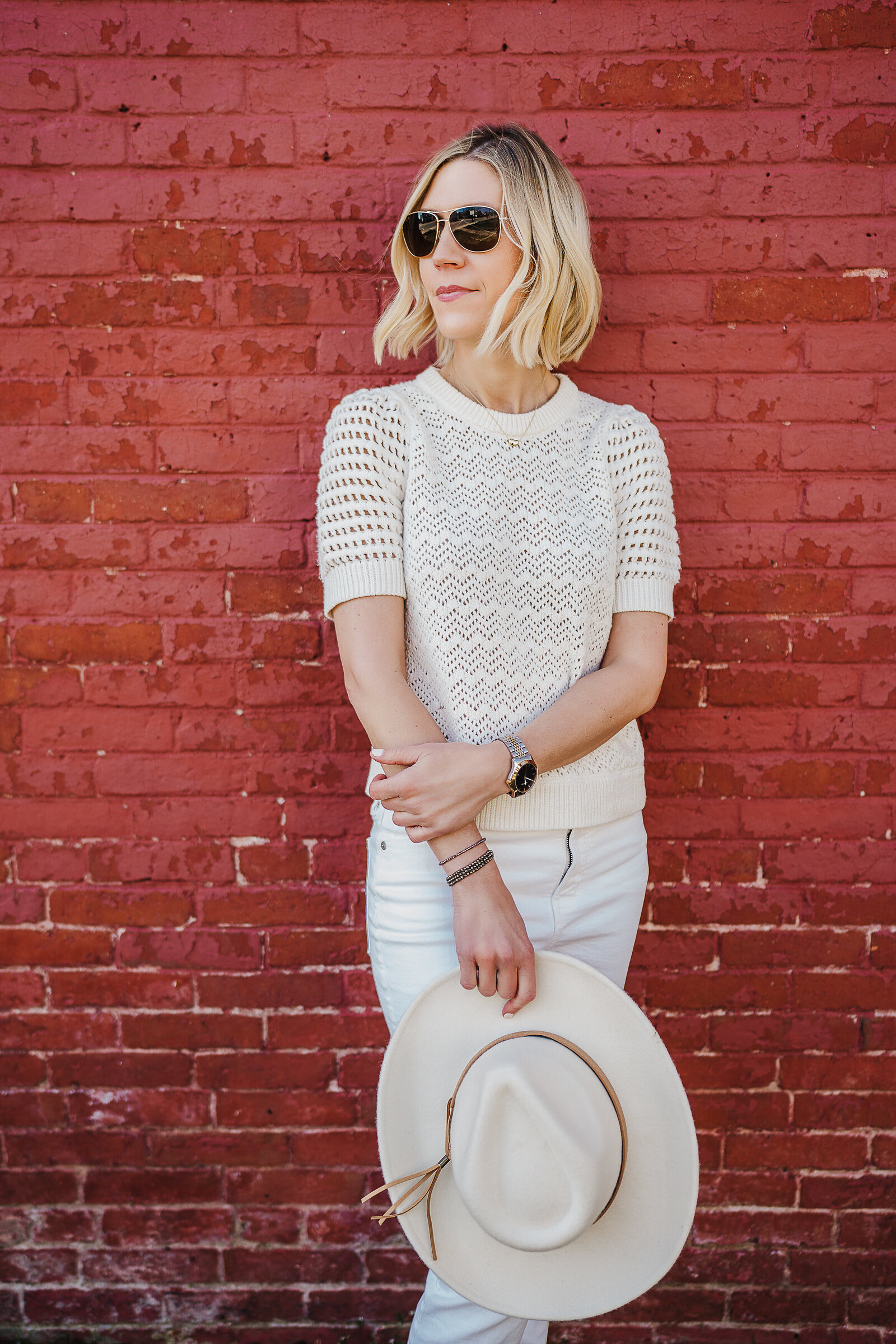 woman stands against red brick with sunglasses on