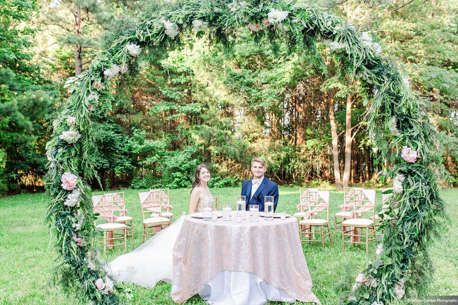 Bride and groom sitting at a sweetheart table under a floral arch outdoors