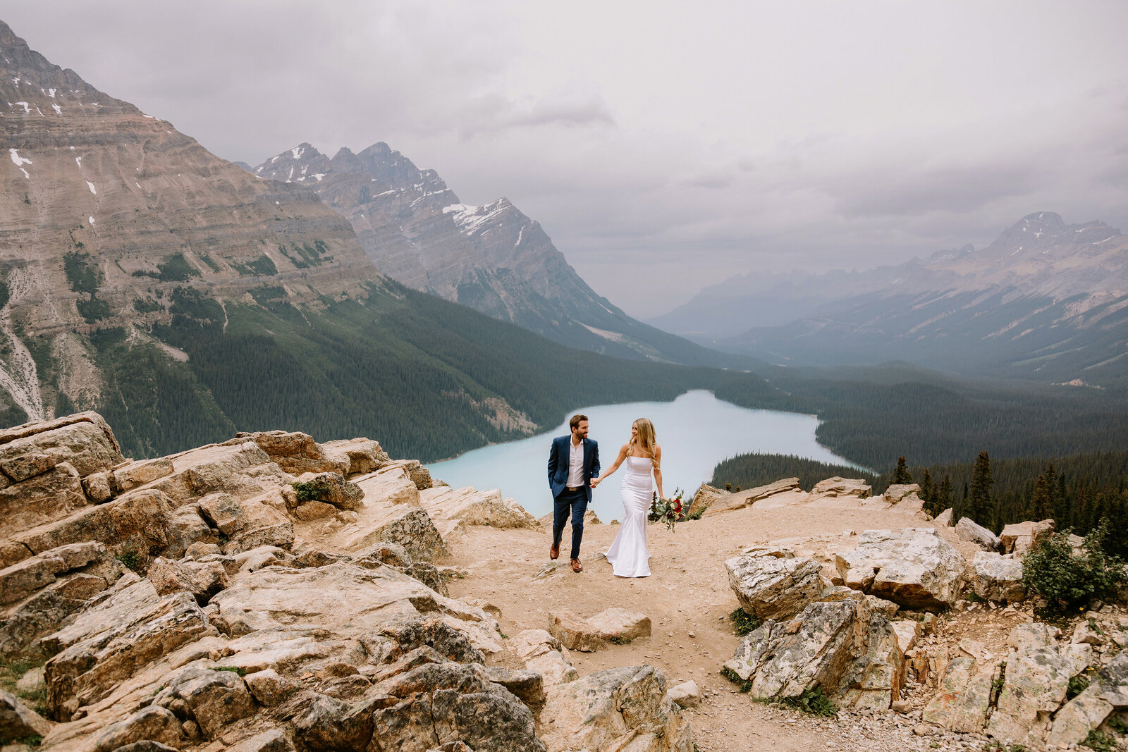 A bride and groom walk along the rocks at Peyto Lake in Banff, Alberta