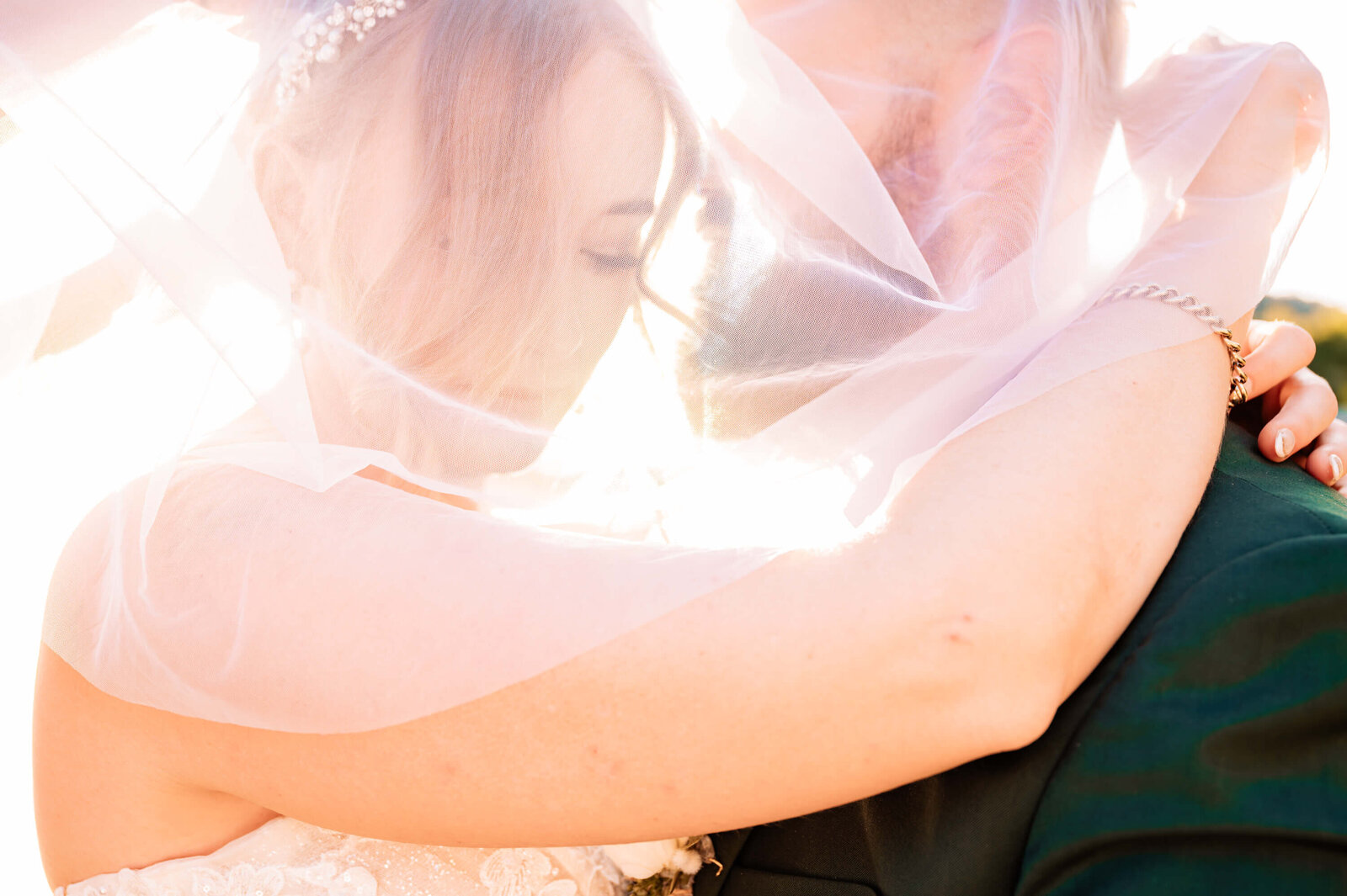 A bride and groom share a tender embrace, their faces partially hidden beneath a delicate veil, symbolizing love and unity.
