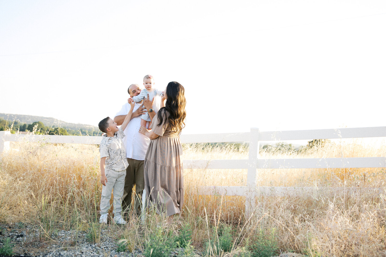 Image of family standing in field looking at baby sister taken by Family Photographer Sacramento Kelsey Krall