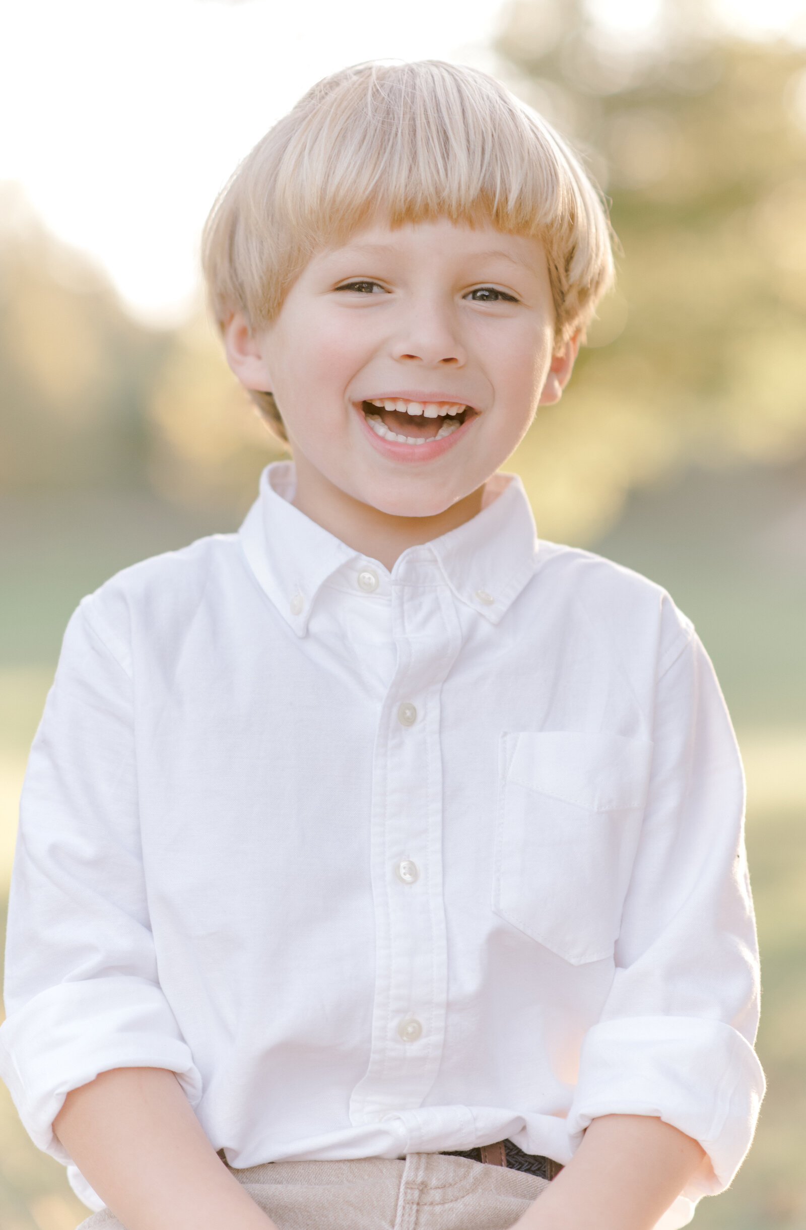 Young blonde boy smiling for portrait in Houston with sun setting behind him.