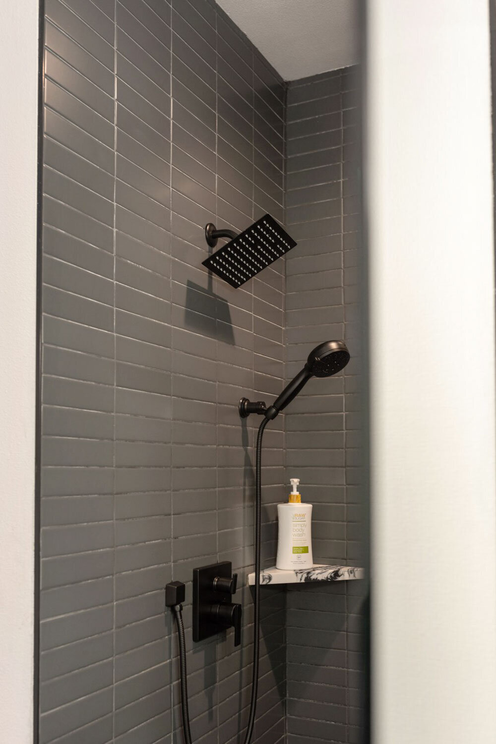 Dark tiled shower with black fixtures and a hand-held sprayer