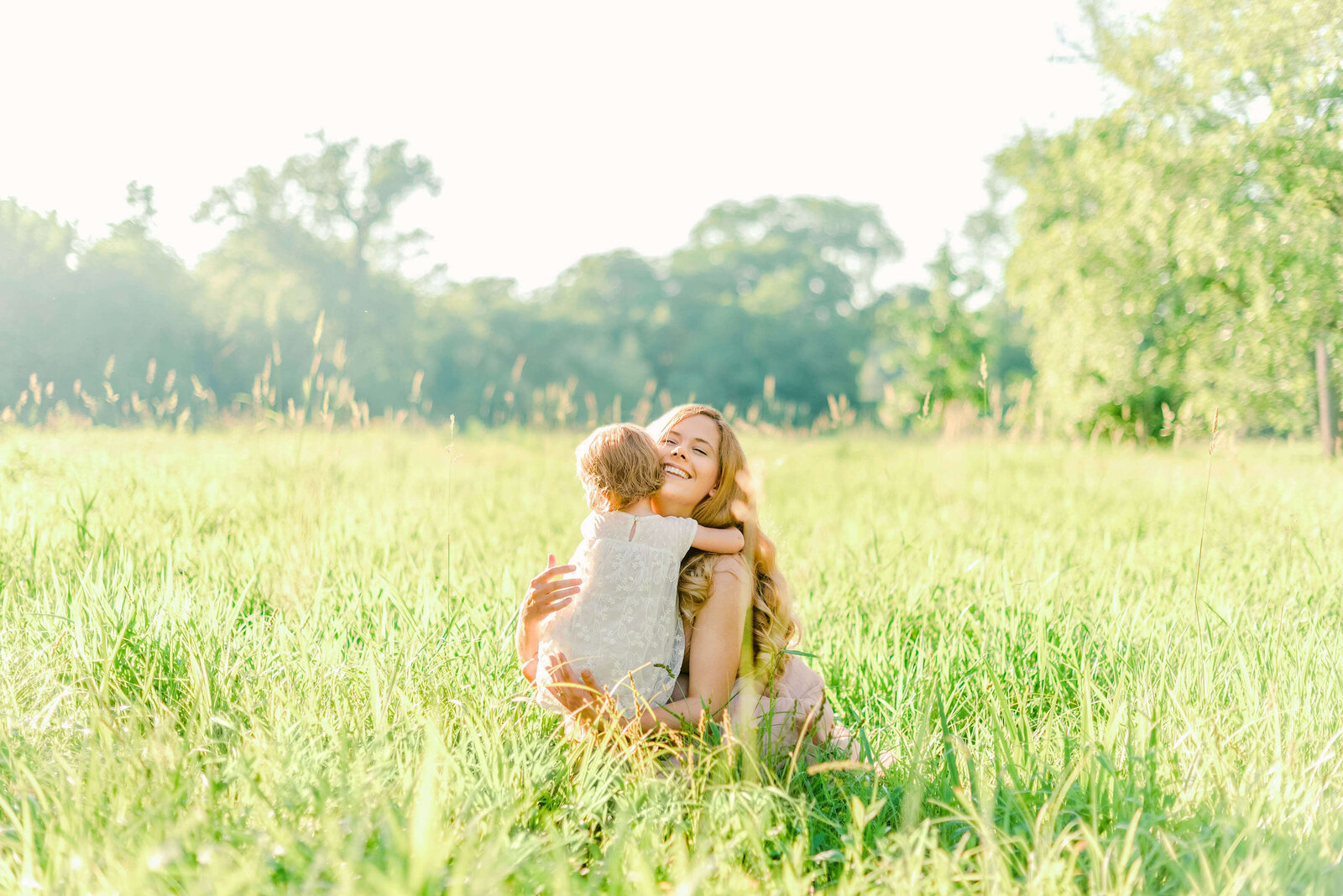 Toddler daughter hugging her mother in a grassy field by Chicago family photographer Kristen Hazelton