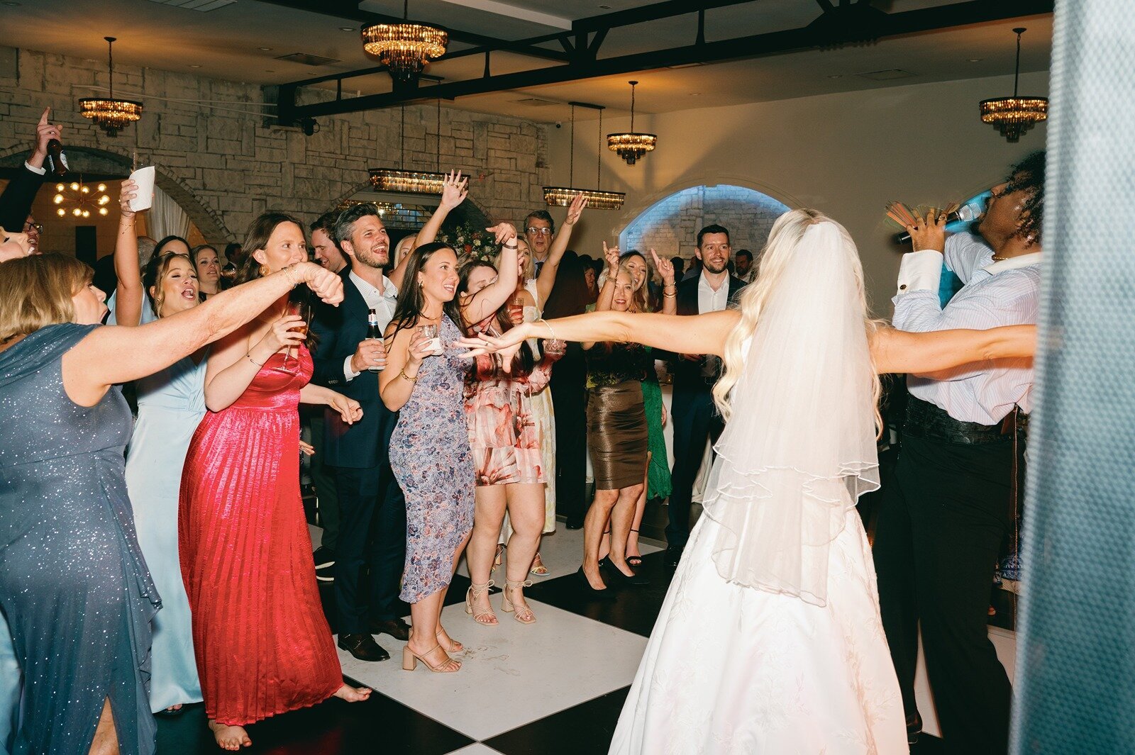 Bride in a white gown leads a group of dancing wedding guests in the luxe room wedding reception