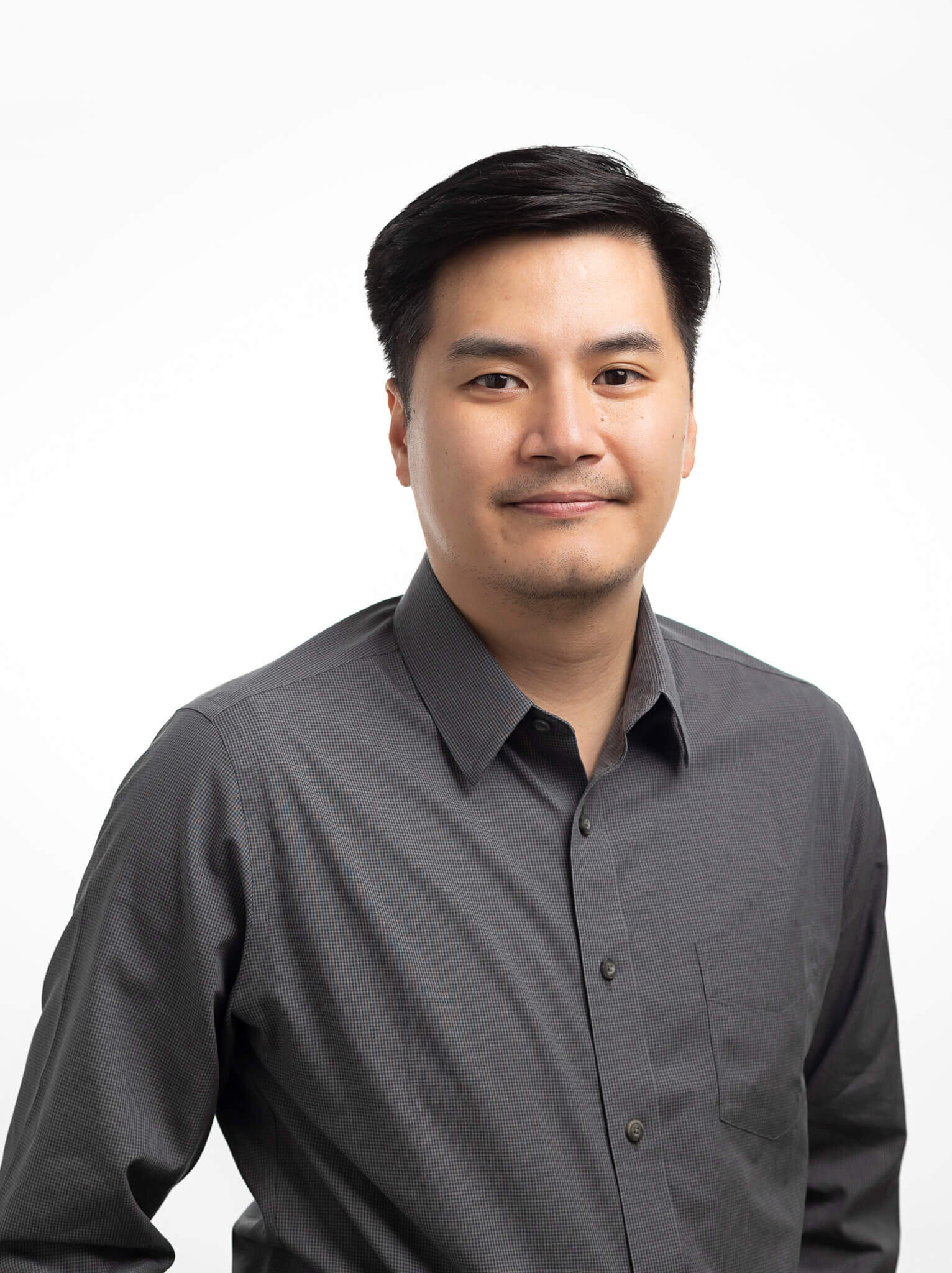 Asian man is posing over a white backdrop in a relaxed and professional way in Austin Texas