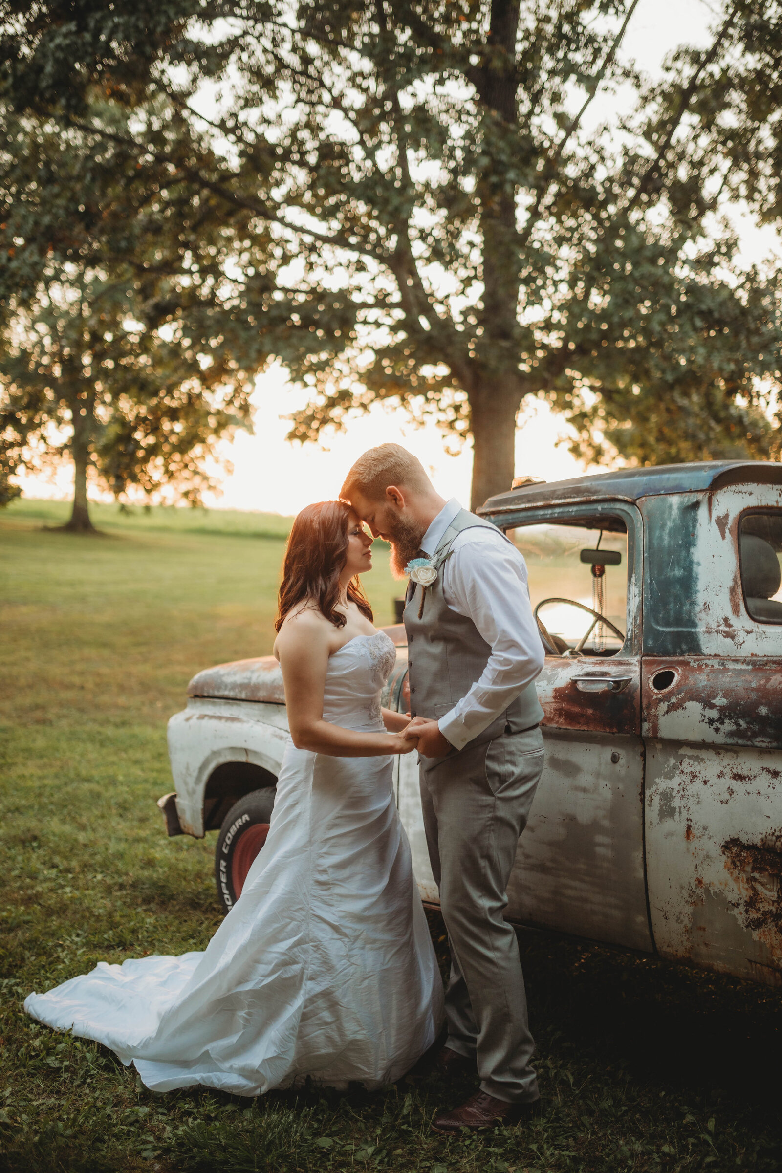 Bride and Groom embracing at sunset by a vintage truck on a field in Blacksburg, Virginia. Captured by Melena Lawson.