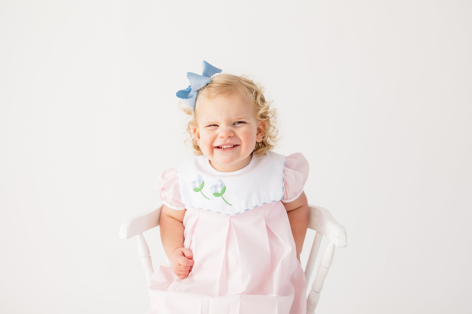 Little girl smiling and scrunching up her nose while she sits in a white chair