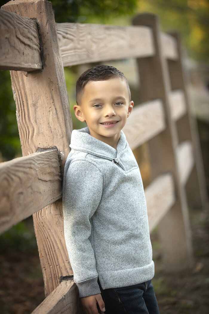 Boy smiling on rustic fence, a Dallas Family Photographer