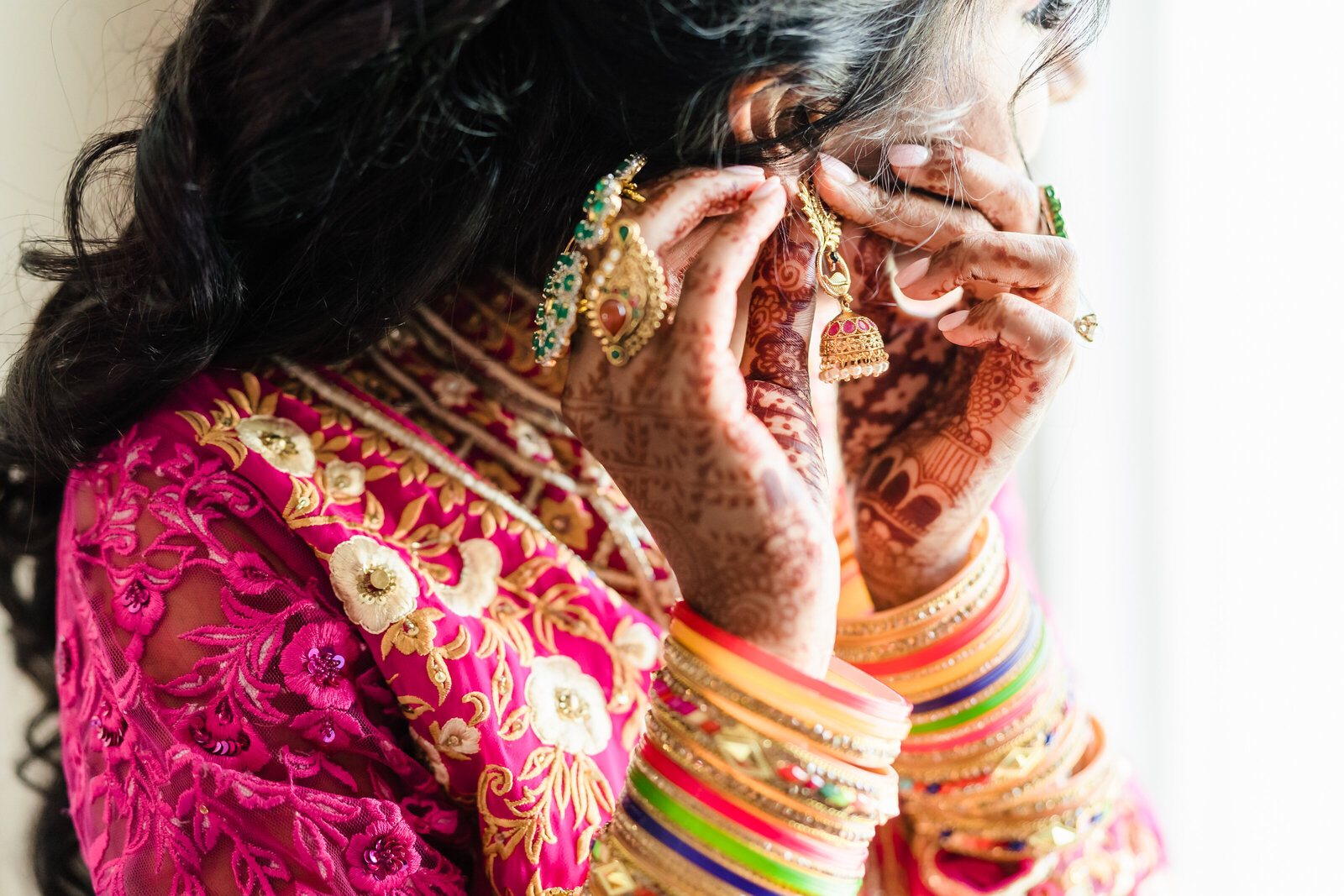 A South Asian bride puts on her earring, showing off her henna