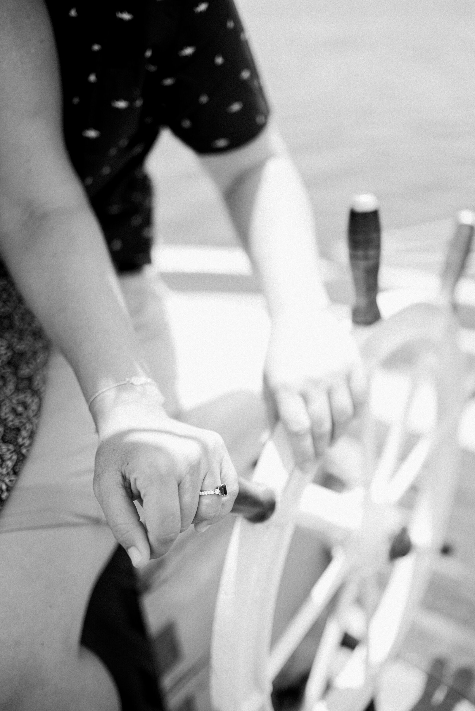 black and white close up photograph of engaged couples hands on the steering helm of a sailboat. Engagement ring is on full display