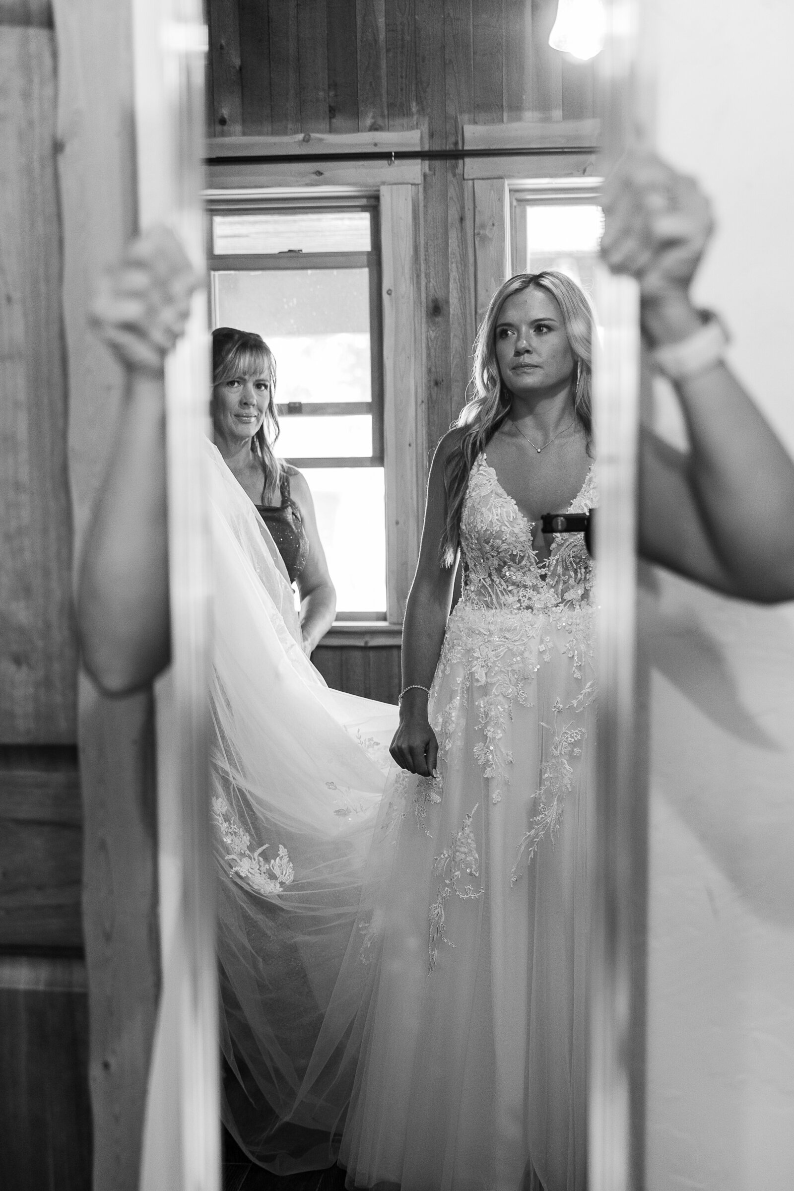 Black and white image of bride looking in the mirror at the cabin in Arrowhead, CO