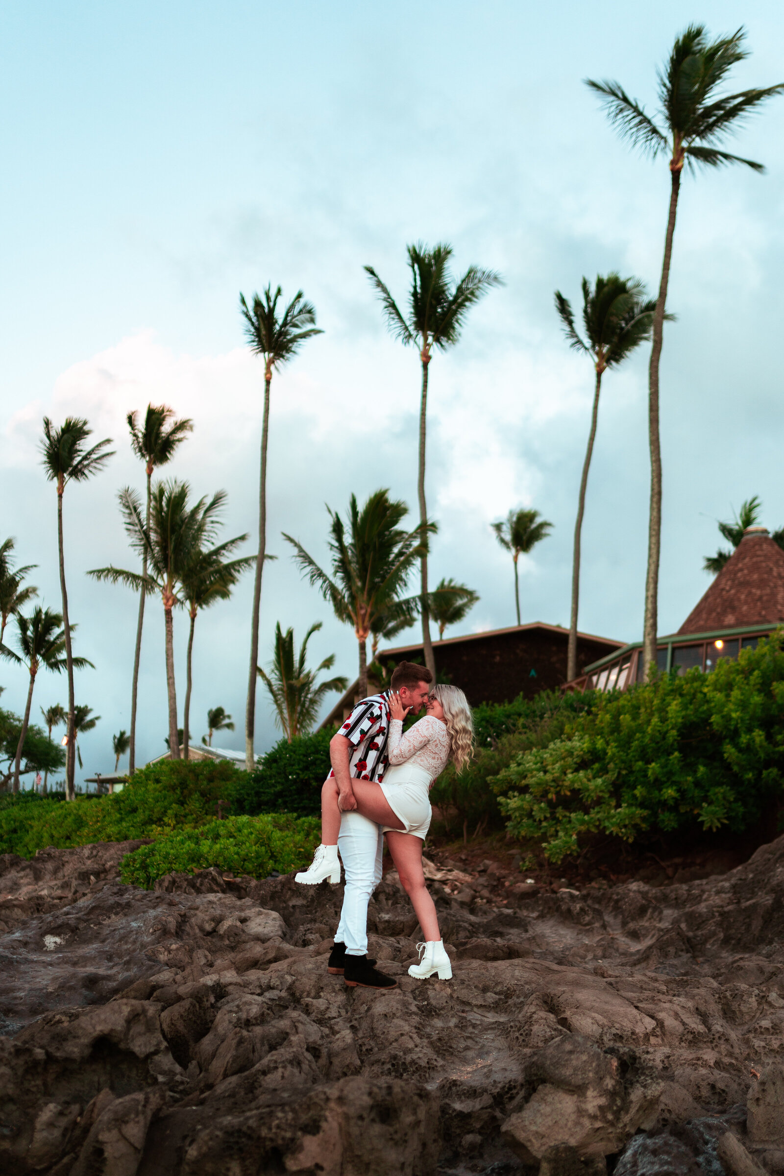 Couple standing on rock kissing with palm trees in the background.