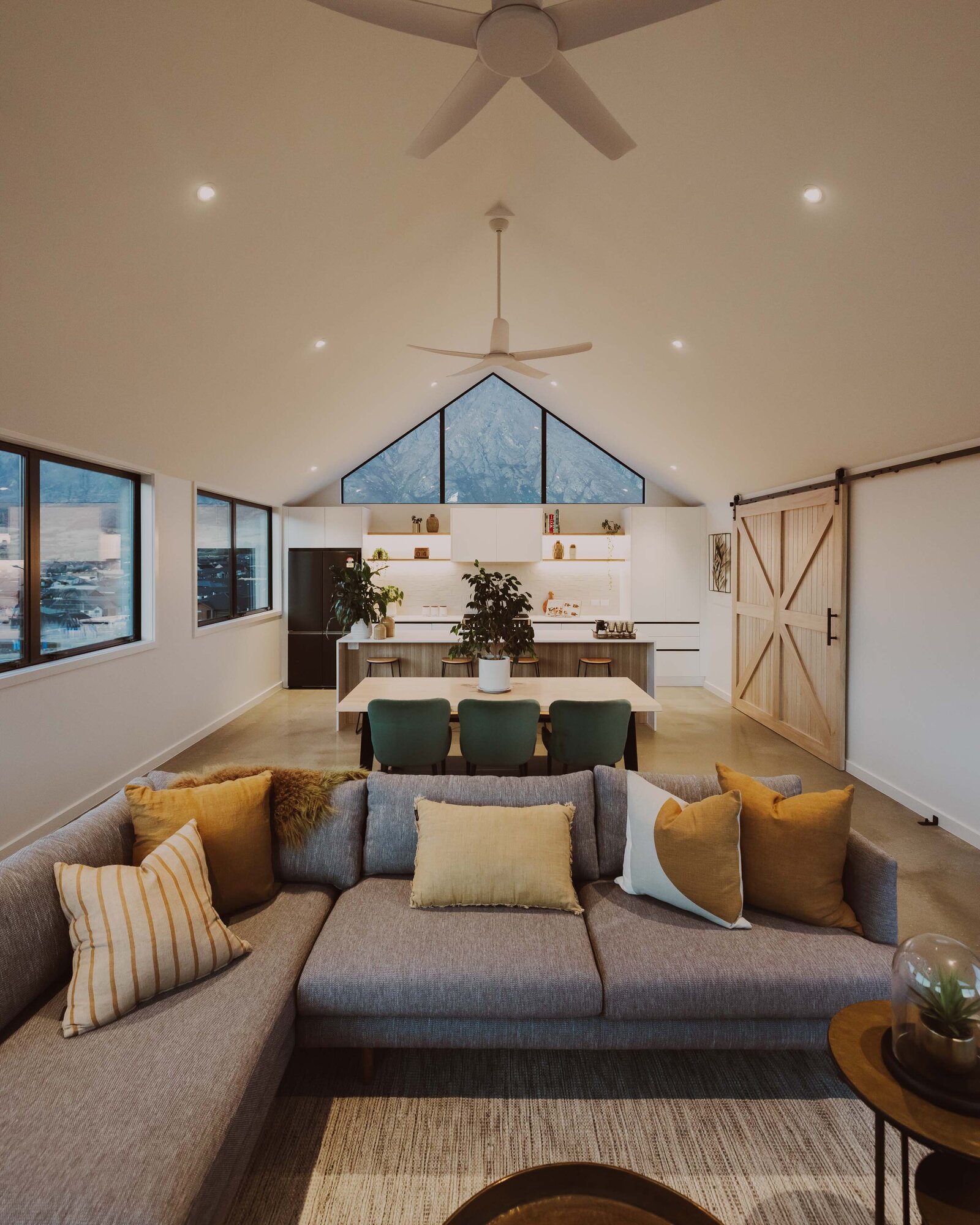 A bright and open plan living area with pitched ceilings, timber barn door, and well-lit kitchen in a home built by Twin Peaks Construction in Hanleys Farm, Queenstown.