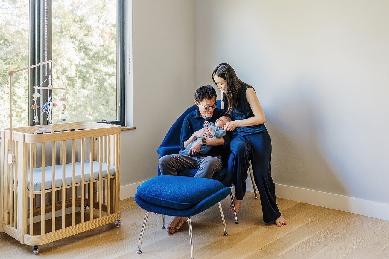 new parents lean over newborn in modern chair in nursery
