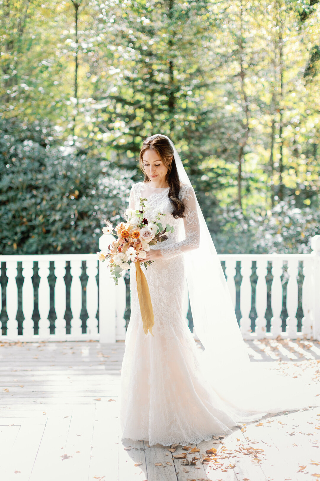 Bride looking at bouquet on porch at The Farm at Old Edwards Inn