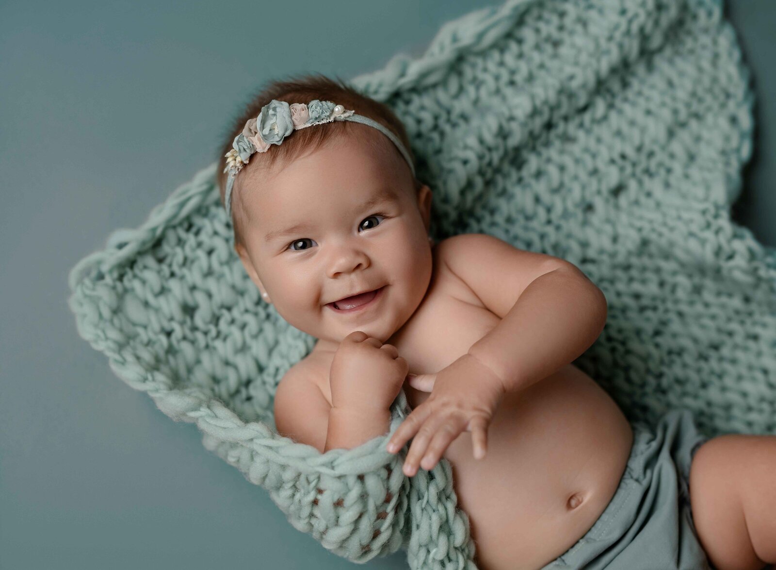 Baby girl laying on her back and playing with blanket and smiling.