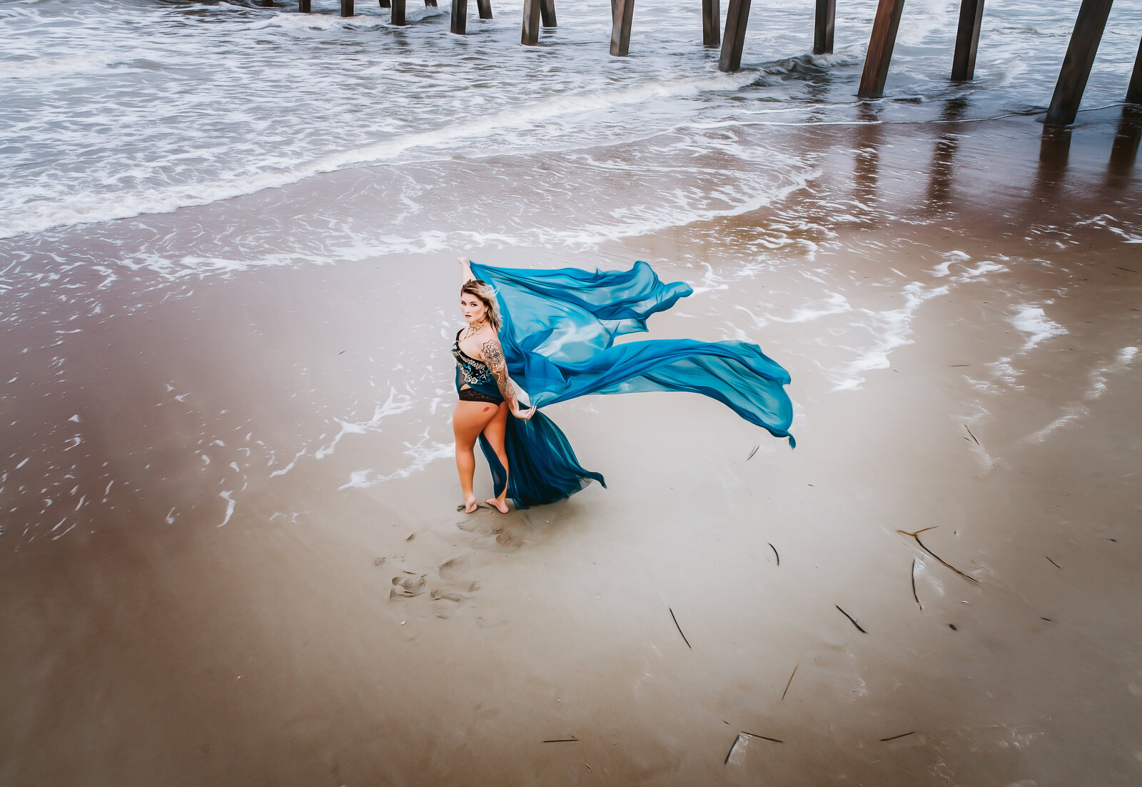 Aerial shot of woman on beach with blue flowy gown