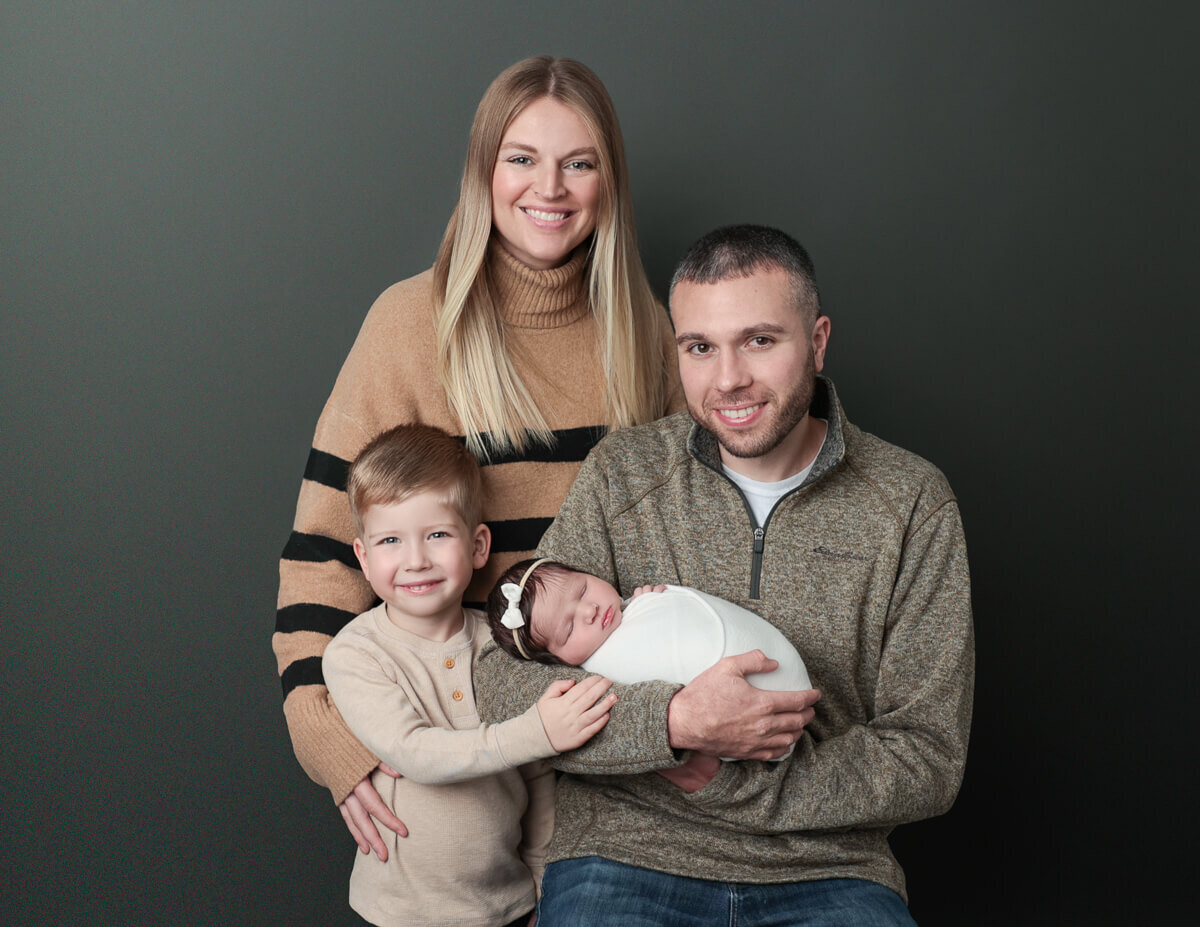 A smiling family poses with their newborn in a cozy living room setting, showcasing love and togetherness in Rochester, NY.