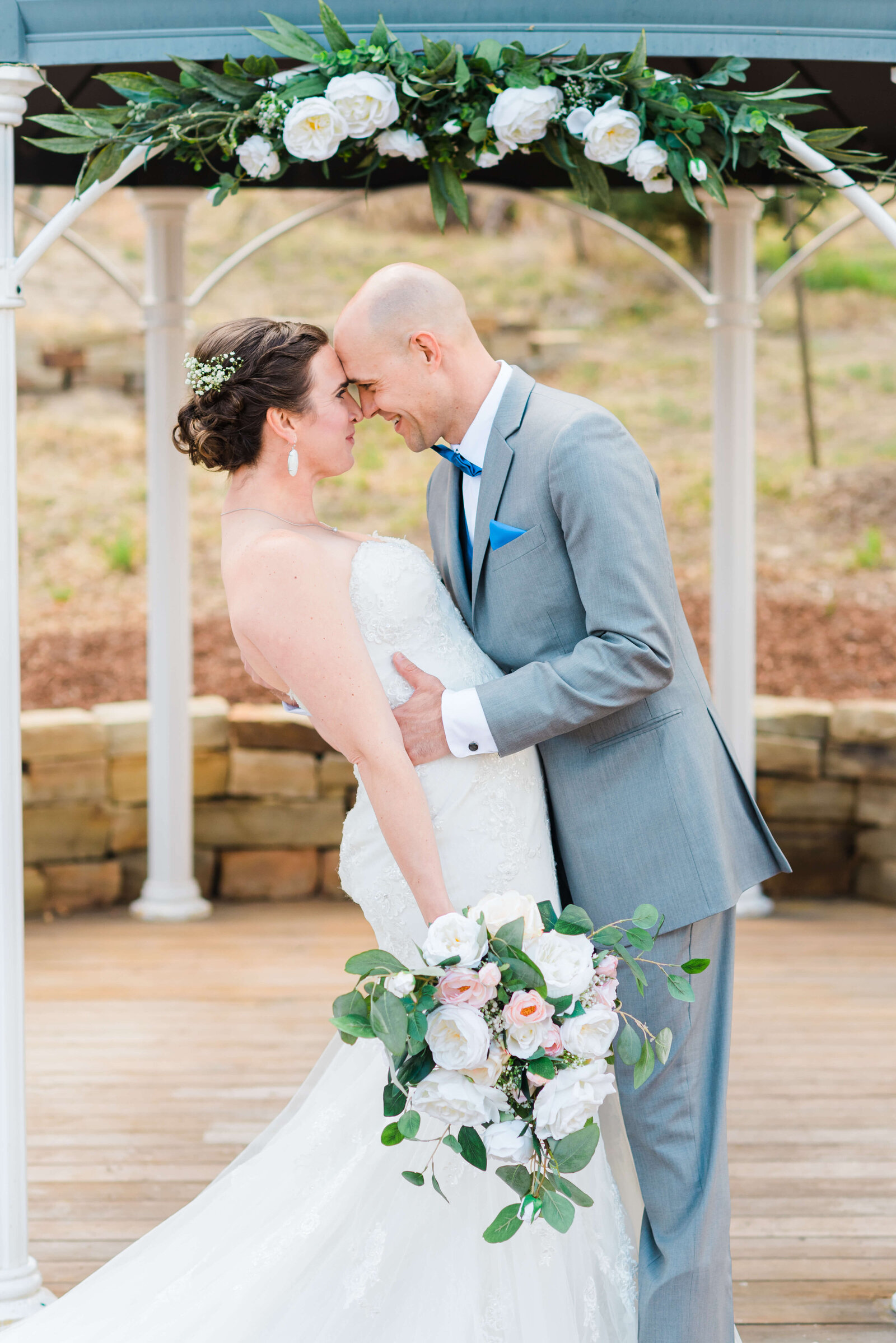 Touching foreheads and smiling at each other, the bride in a white dress and the groom in a grey suit share an intimate moment during a photo captured by Virginia wedding photographer