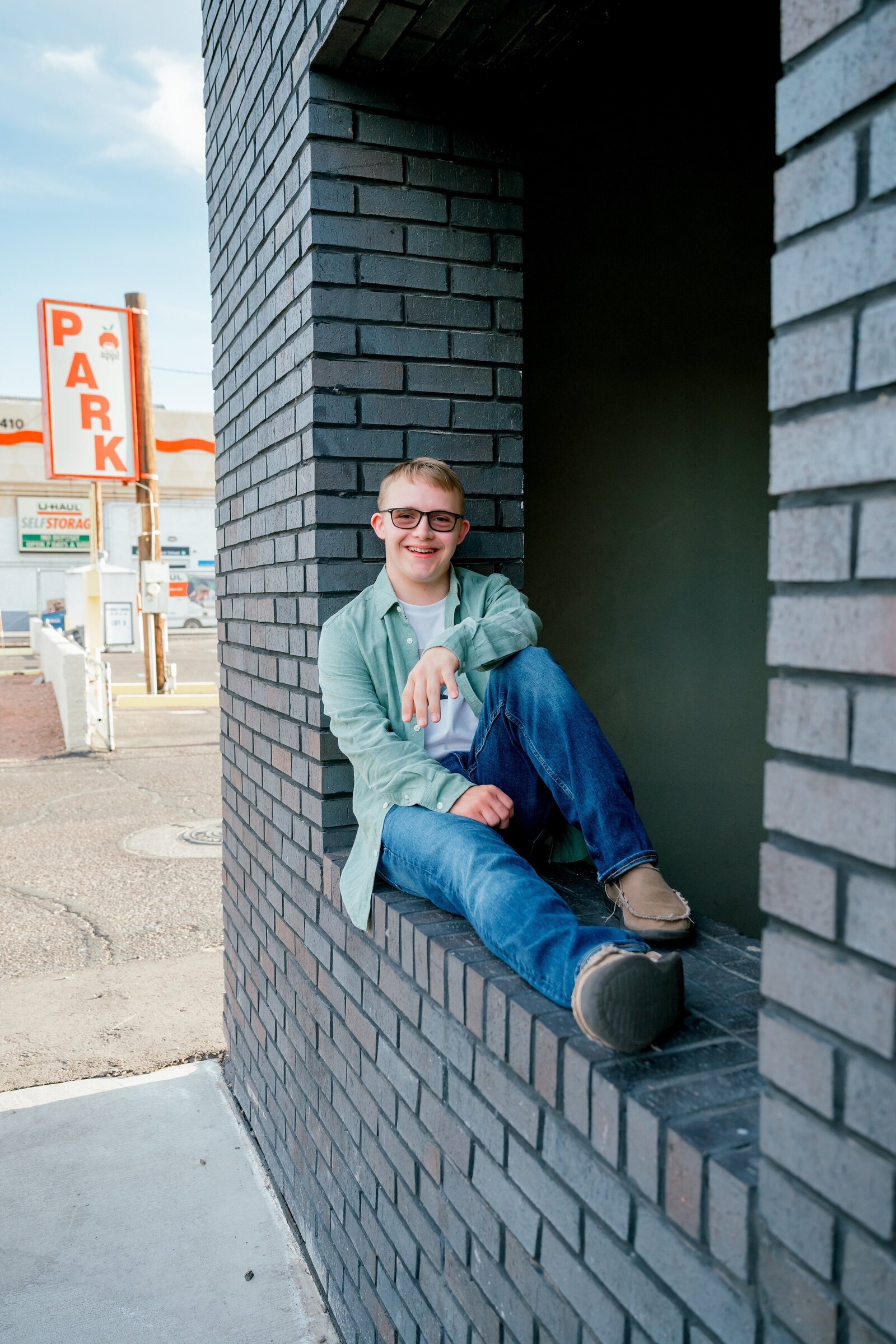senior boy sitting on a brick wall in downtown phoenix smiling at camera 