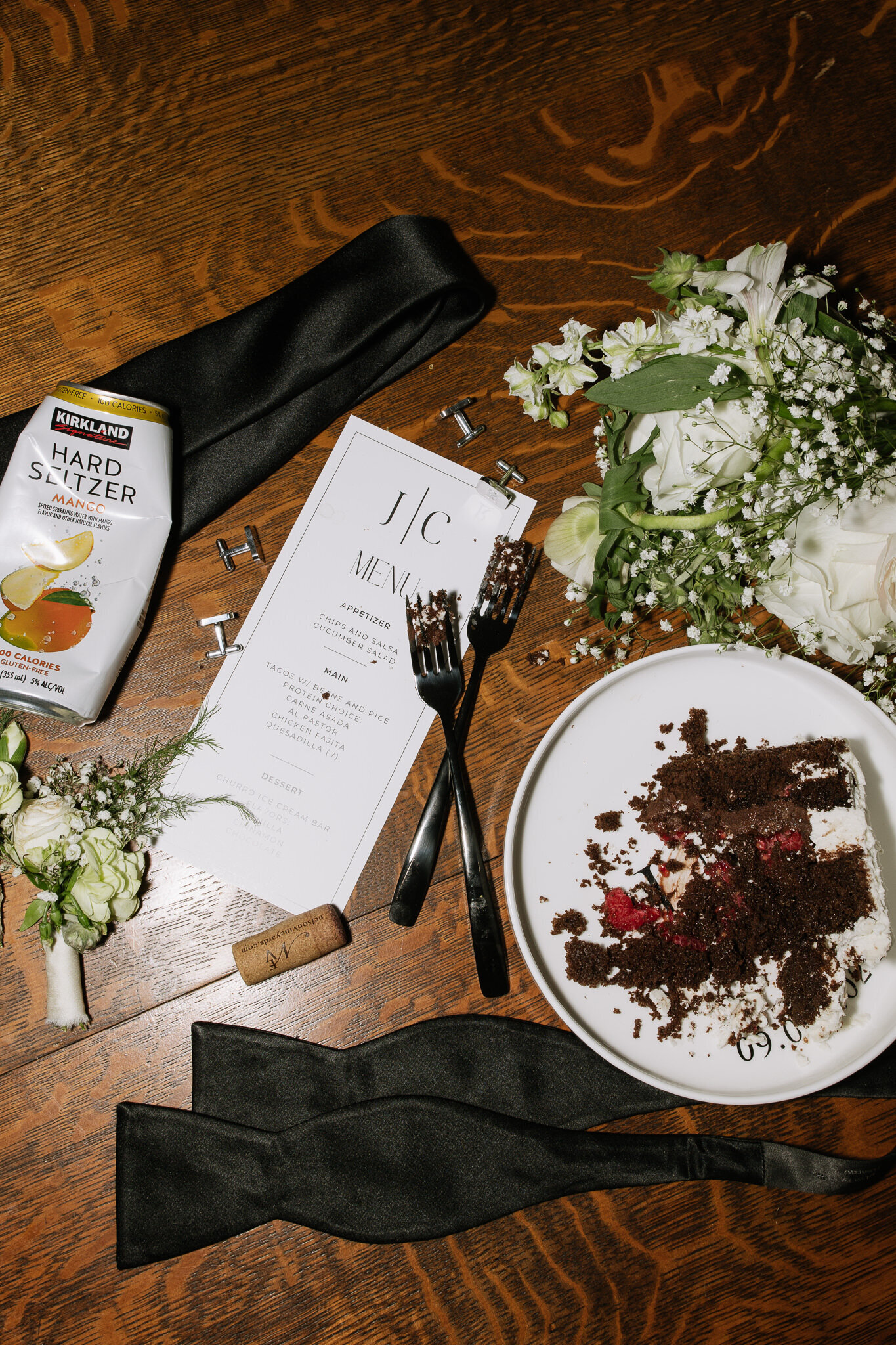 Creative messy flatlay of cake, hard seltzer, florals, and stationary captured with flash during reception