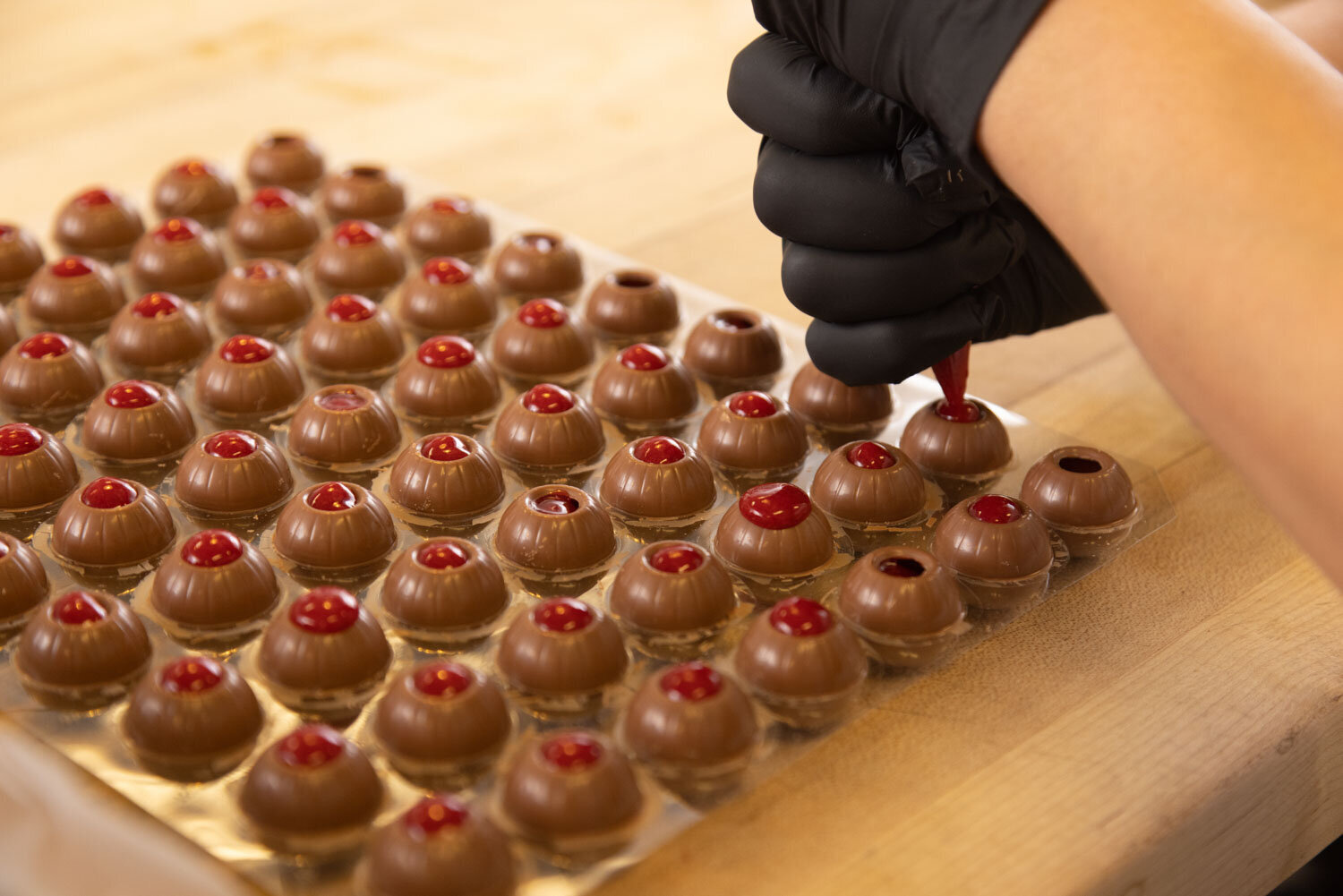 Hand in glove piping filling into rows of chocolate truffles