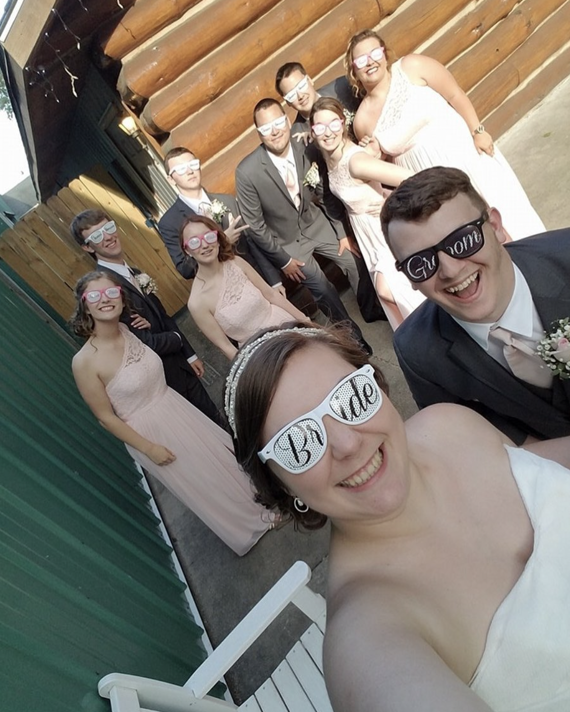 Bride and groom smile for selfie with their wedding parties where bride and groom sunglasses