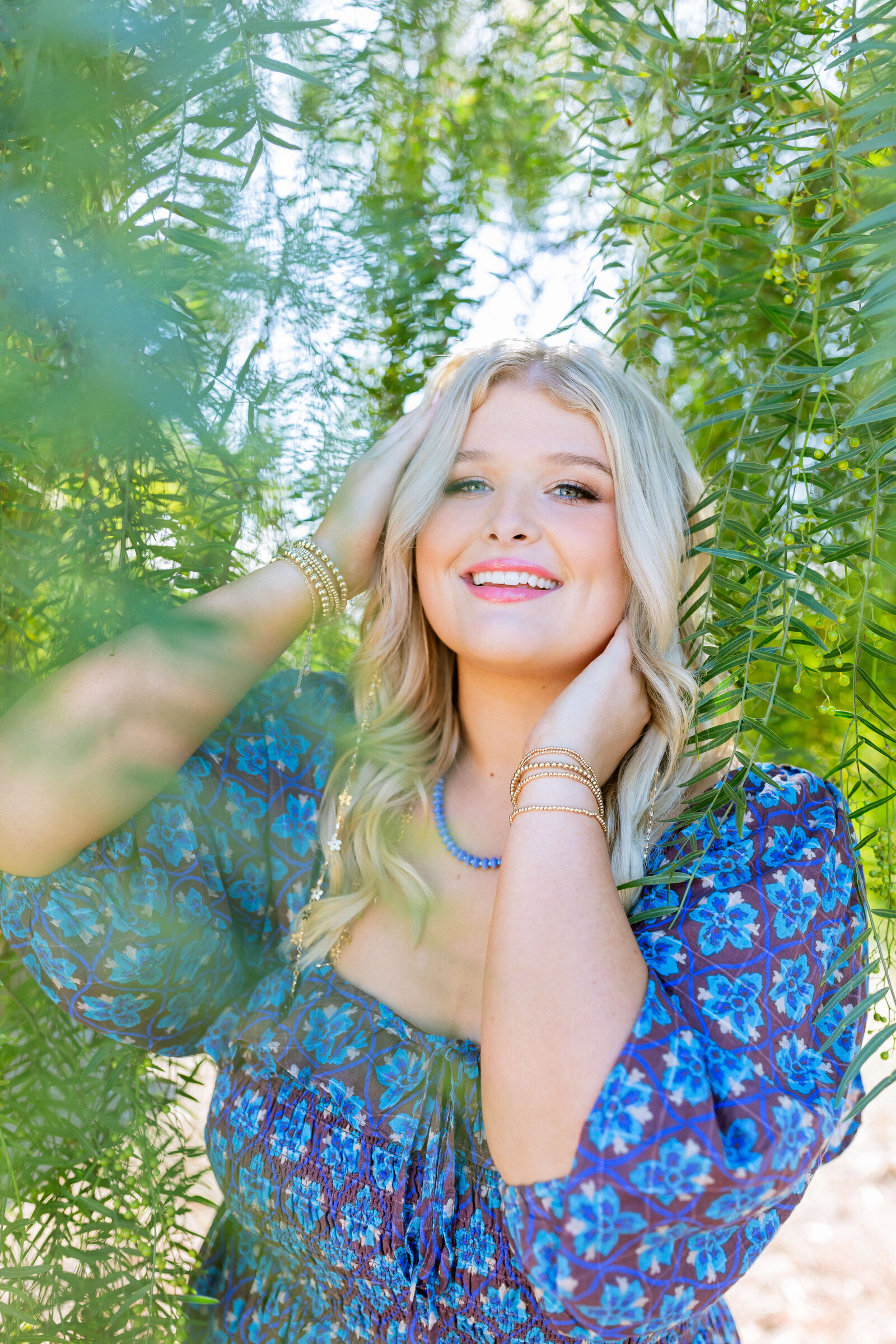 blonde girl wearing blue dress and posing under a tree