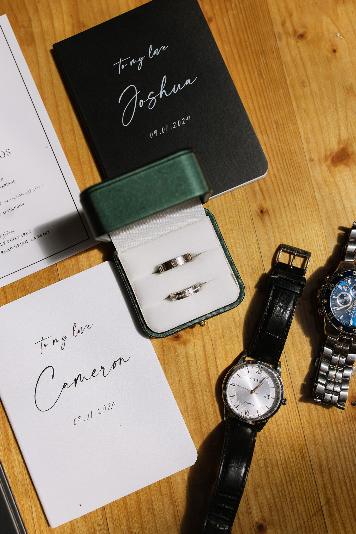 Groom rings and watches displayed with wedding stationary and vow books for flatlay image
